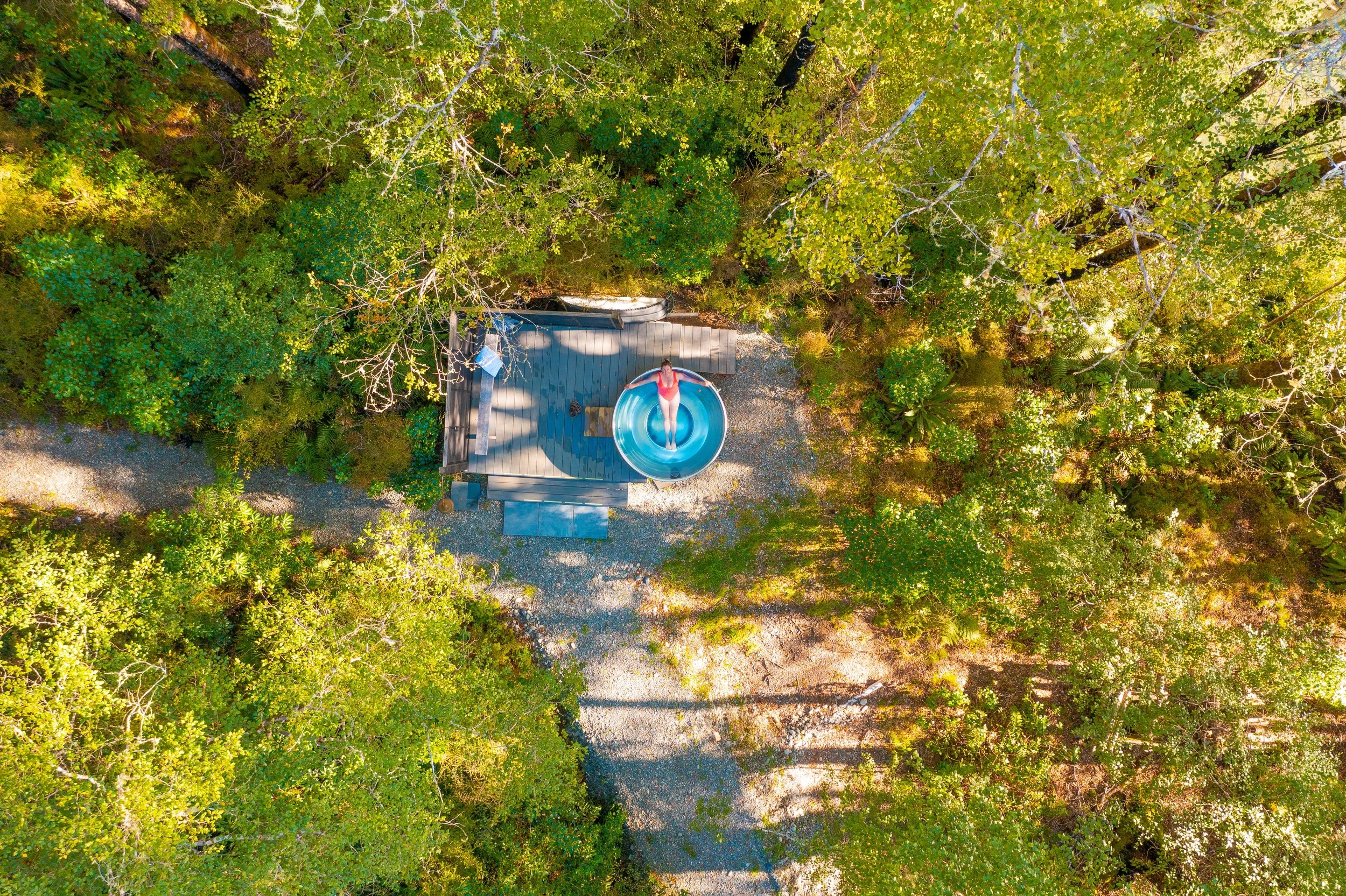 Person swimming in an outdoor pool with lush green trees and mountain landscape in the background.