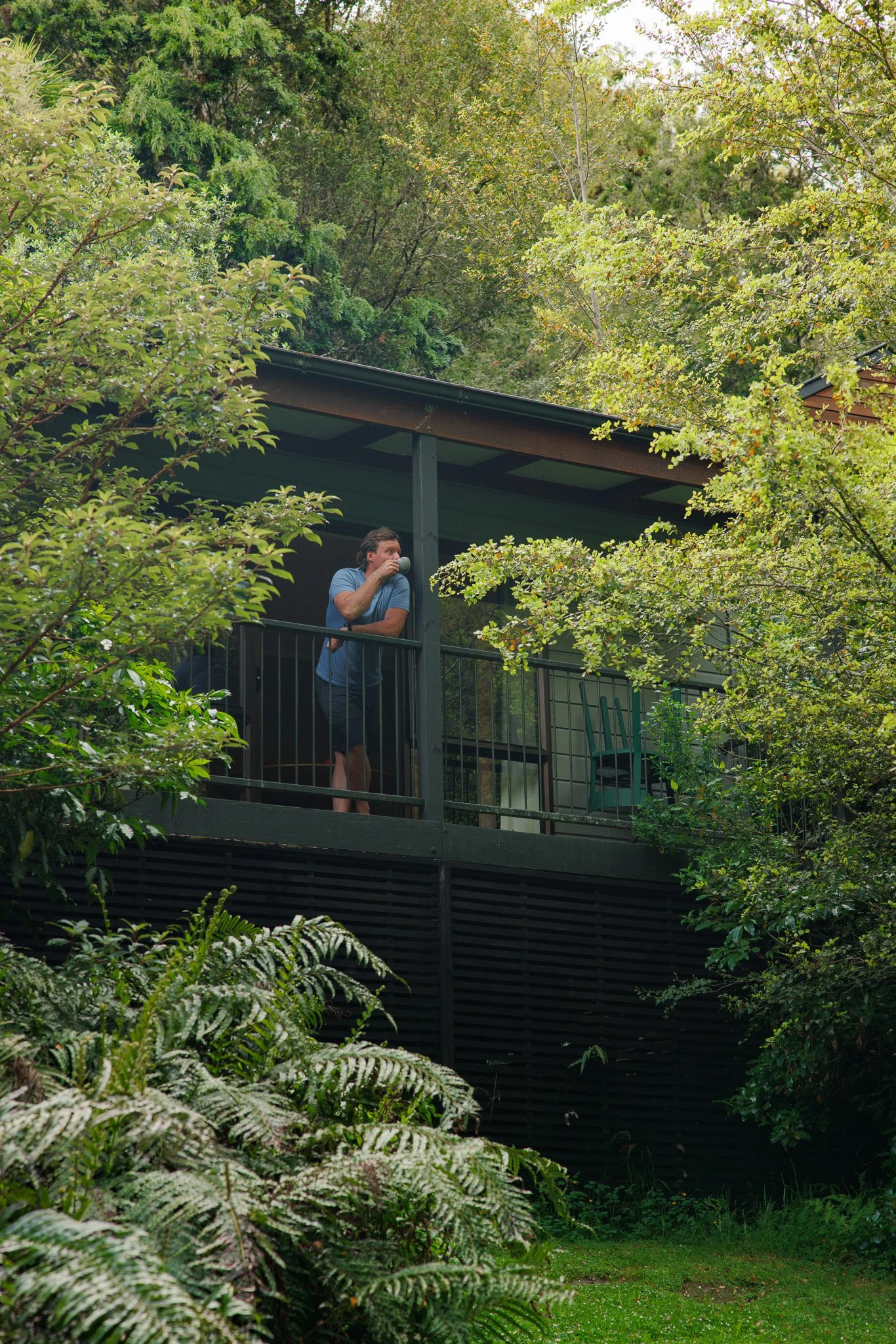 A private villa with a balcony surrounded by lush tropical plants and trees, with a mountain in the background and a partly cloudy sky.