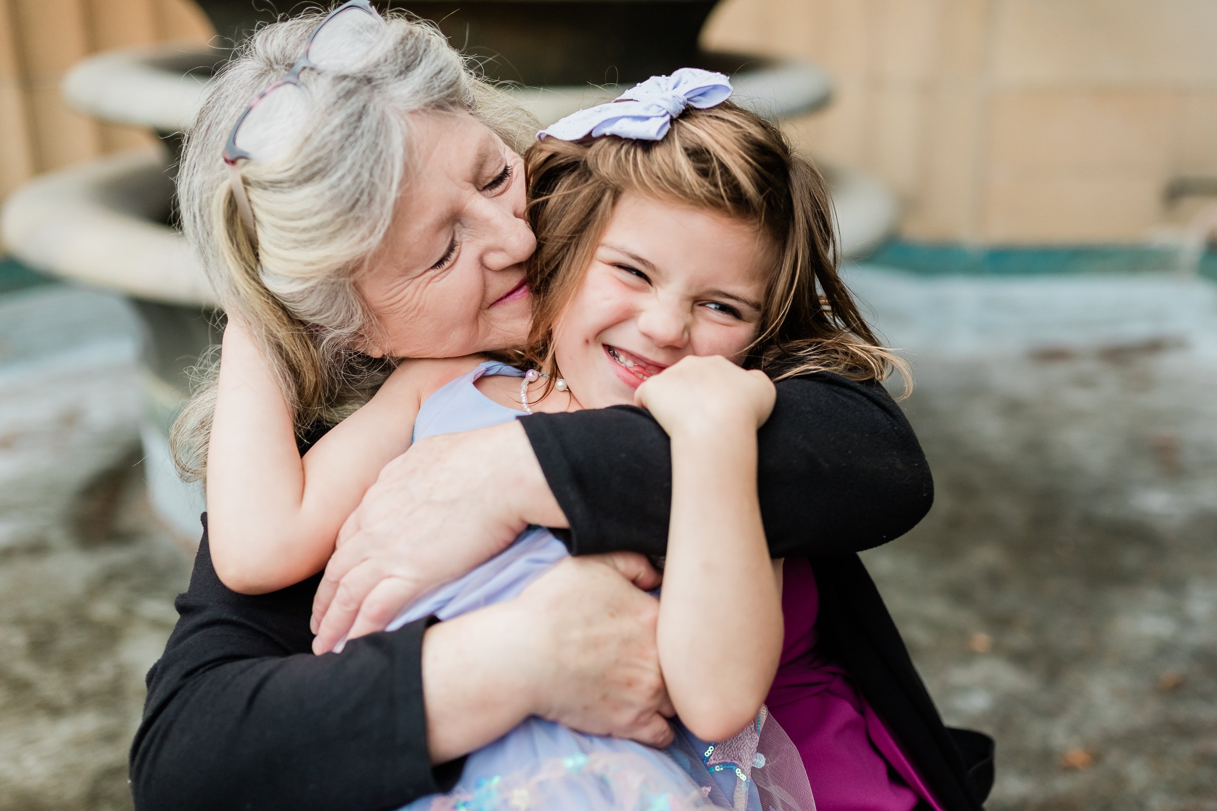  Grandma hugging preschool granddaughter in front of a fountain. 