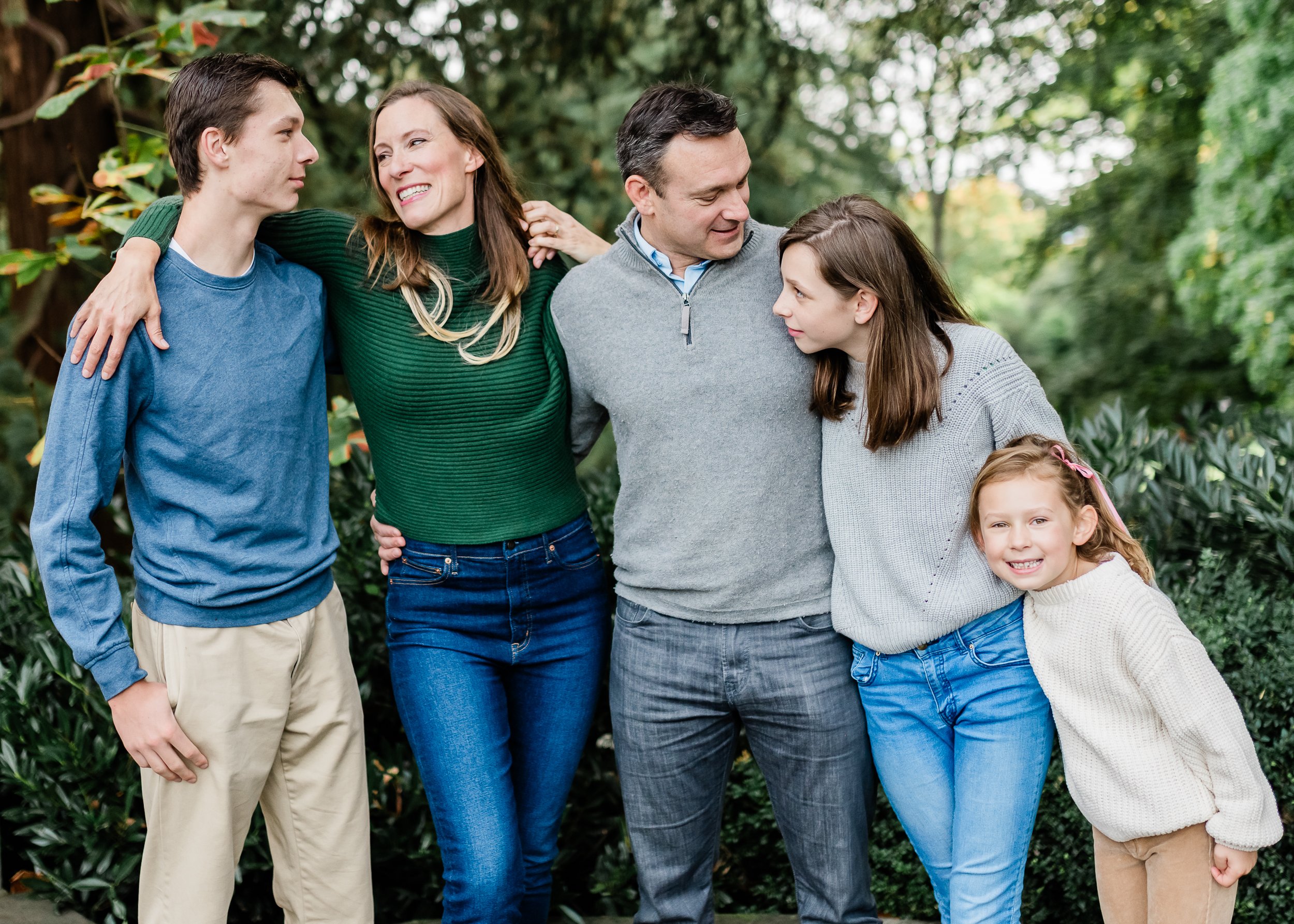  Family of five hugging in front of hedges. 