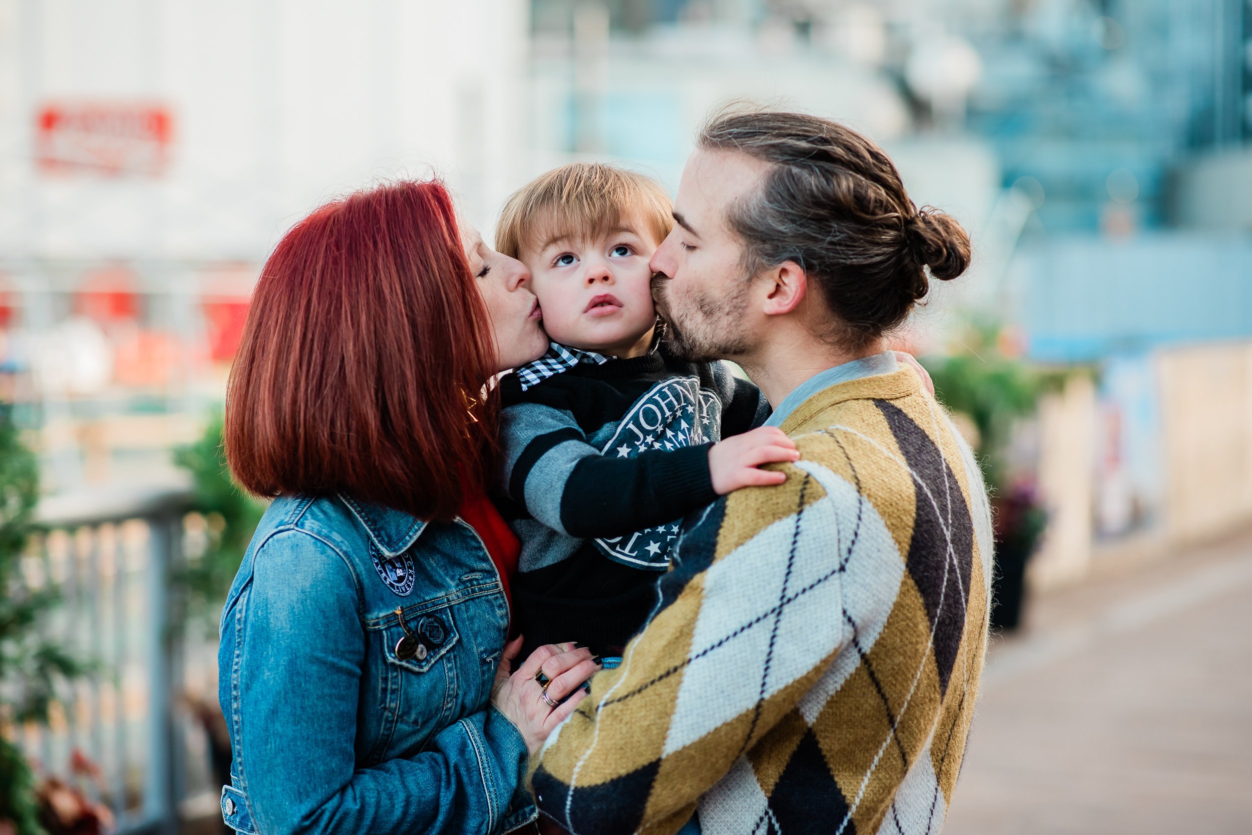  Young mother and father kissing their toddler on the cheek at the same time. 