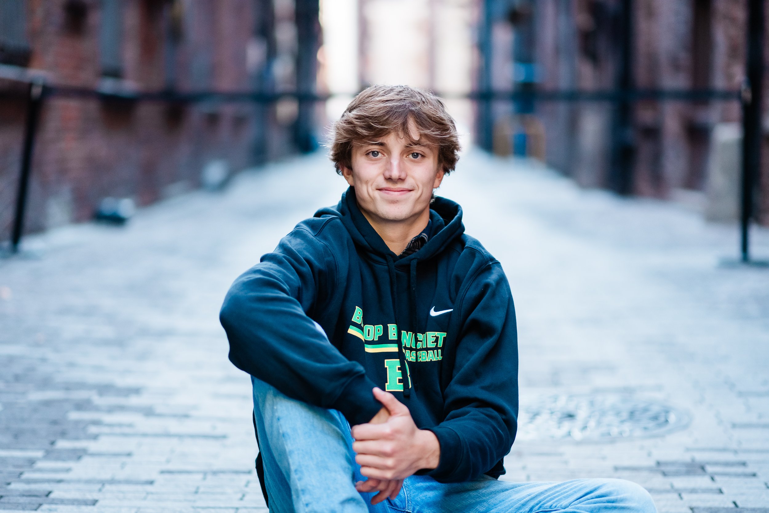  High school senior boy sits on a cobblestone road in Seattle’s Pioneer Square. 