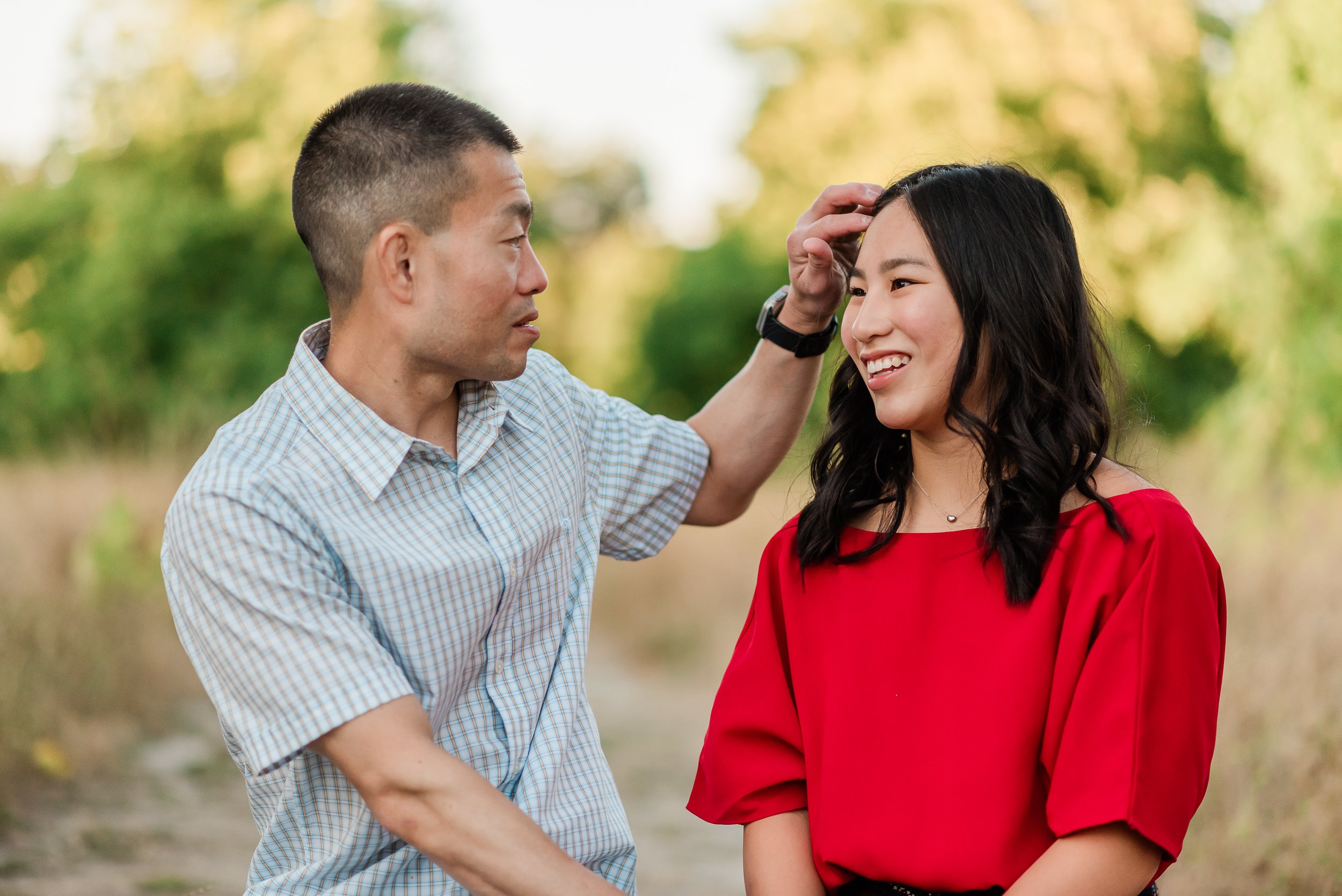  Dad brushes hair out of high school senior daughter’s face during a senior + family session. 
