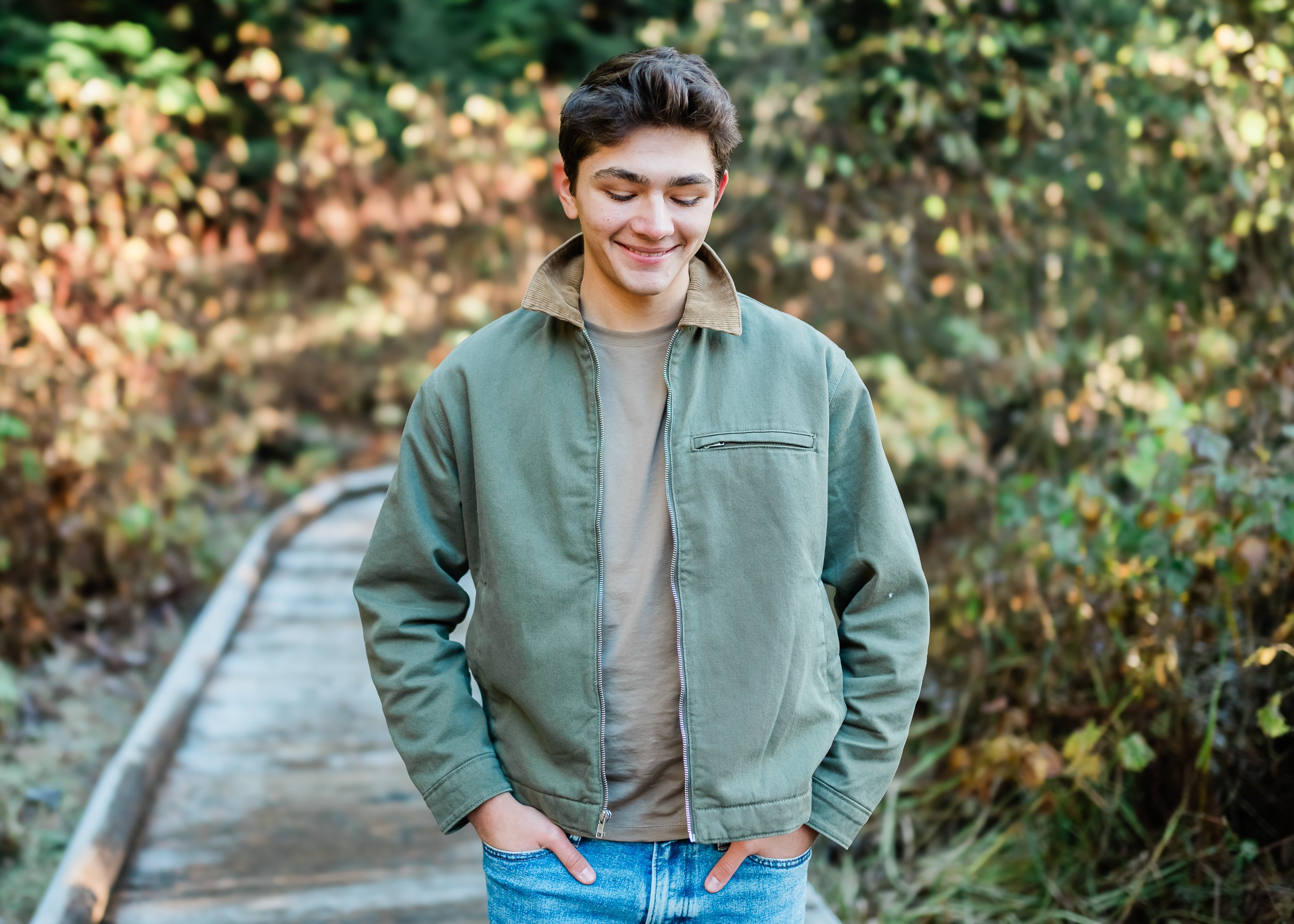  Teenage boy puts his hands in his pockets and smiles at the ground. in the Cascade Mountains. 