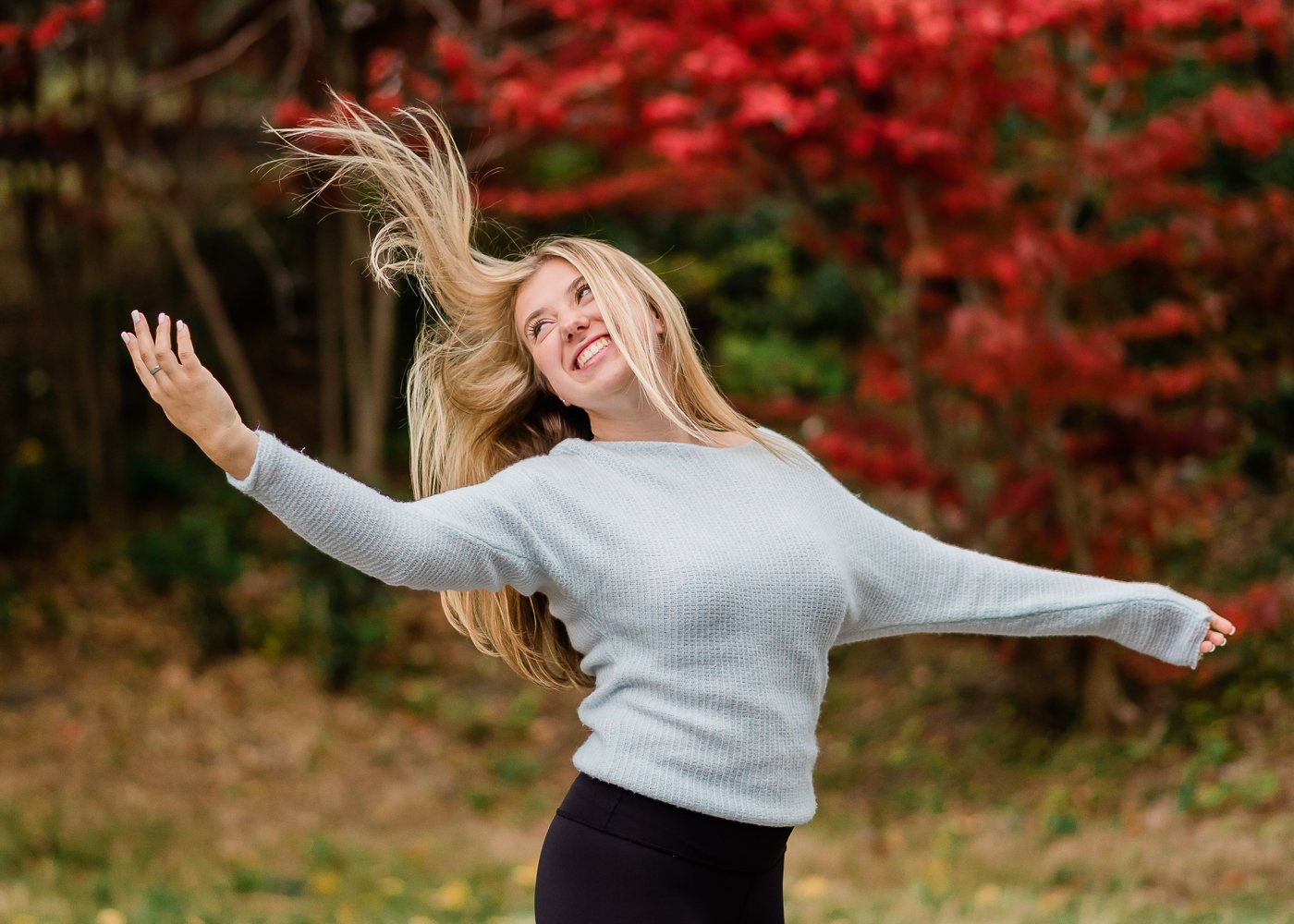  Senior girl flips her hair in front of a red-leafed tree in the fall. 