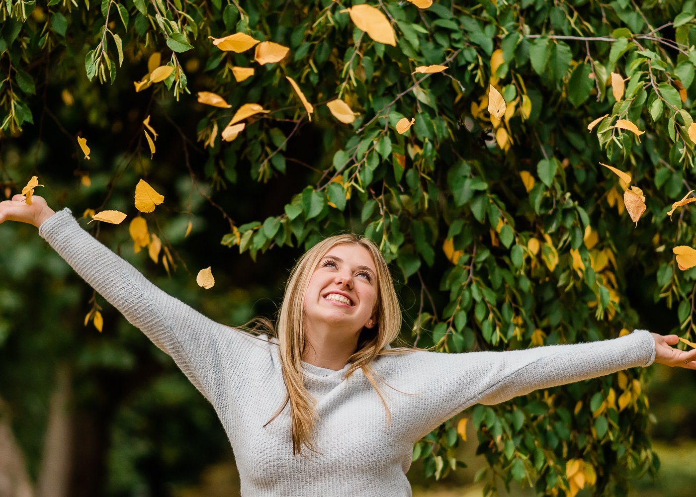  High school senior girl throws leaves in the air during senior. session. 