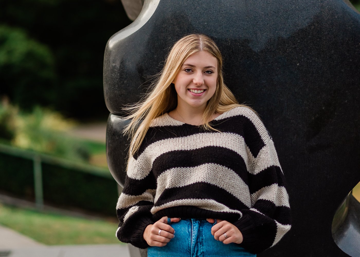  High school senior girl leaning on a statue with hands in her jeans pocket. 