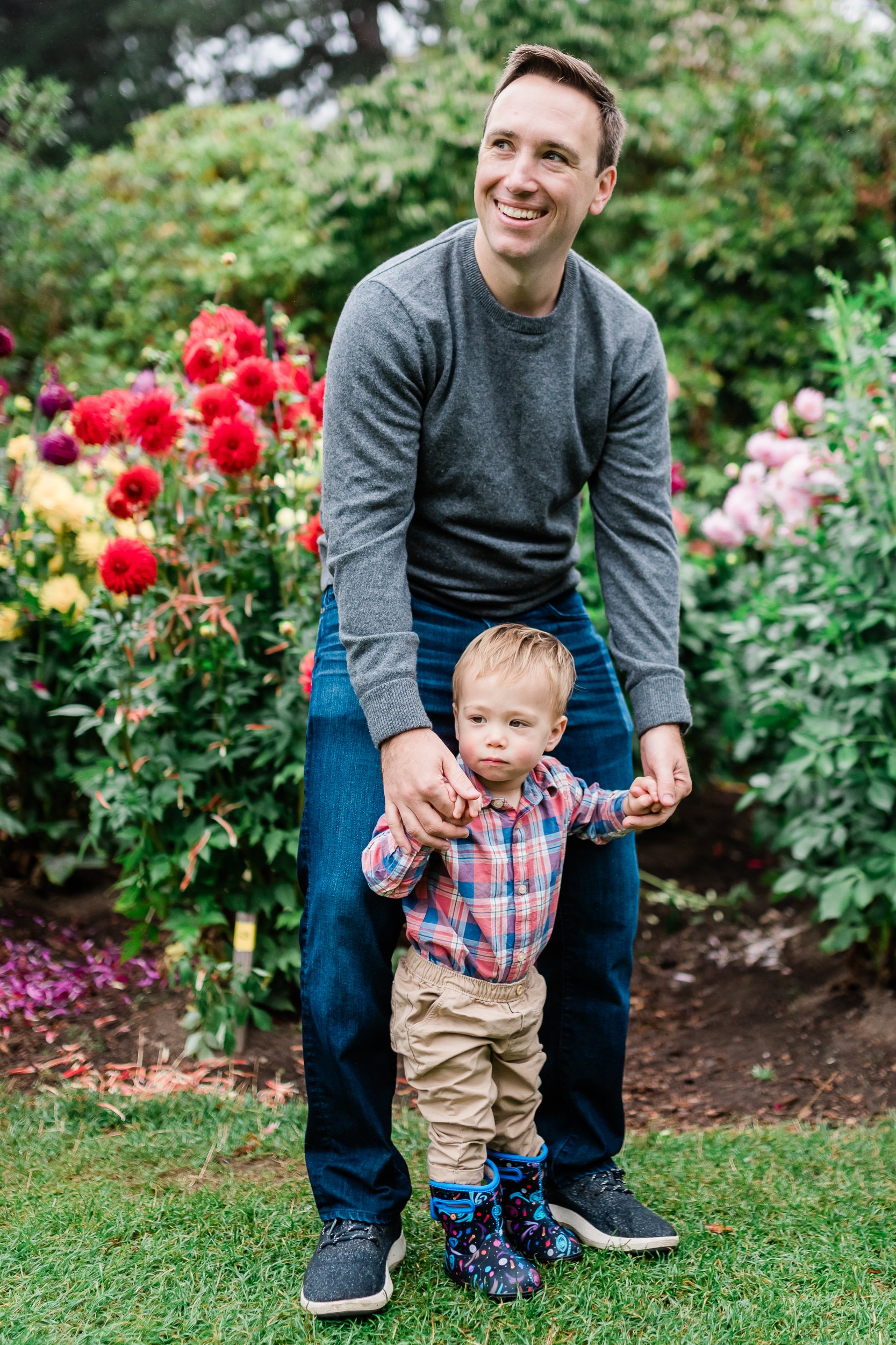  Father and toddler pose and hold hands in a flower garden. 