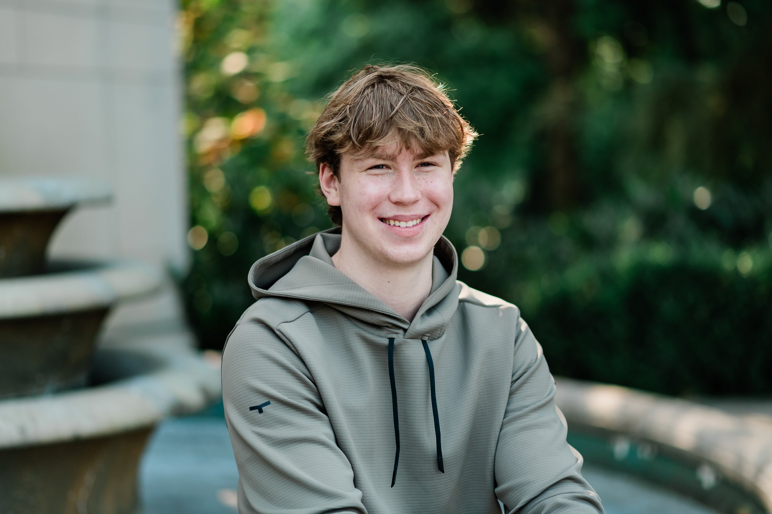  High school senior son poses in front of a fountain. 