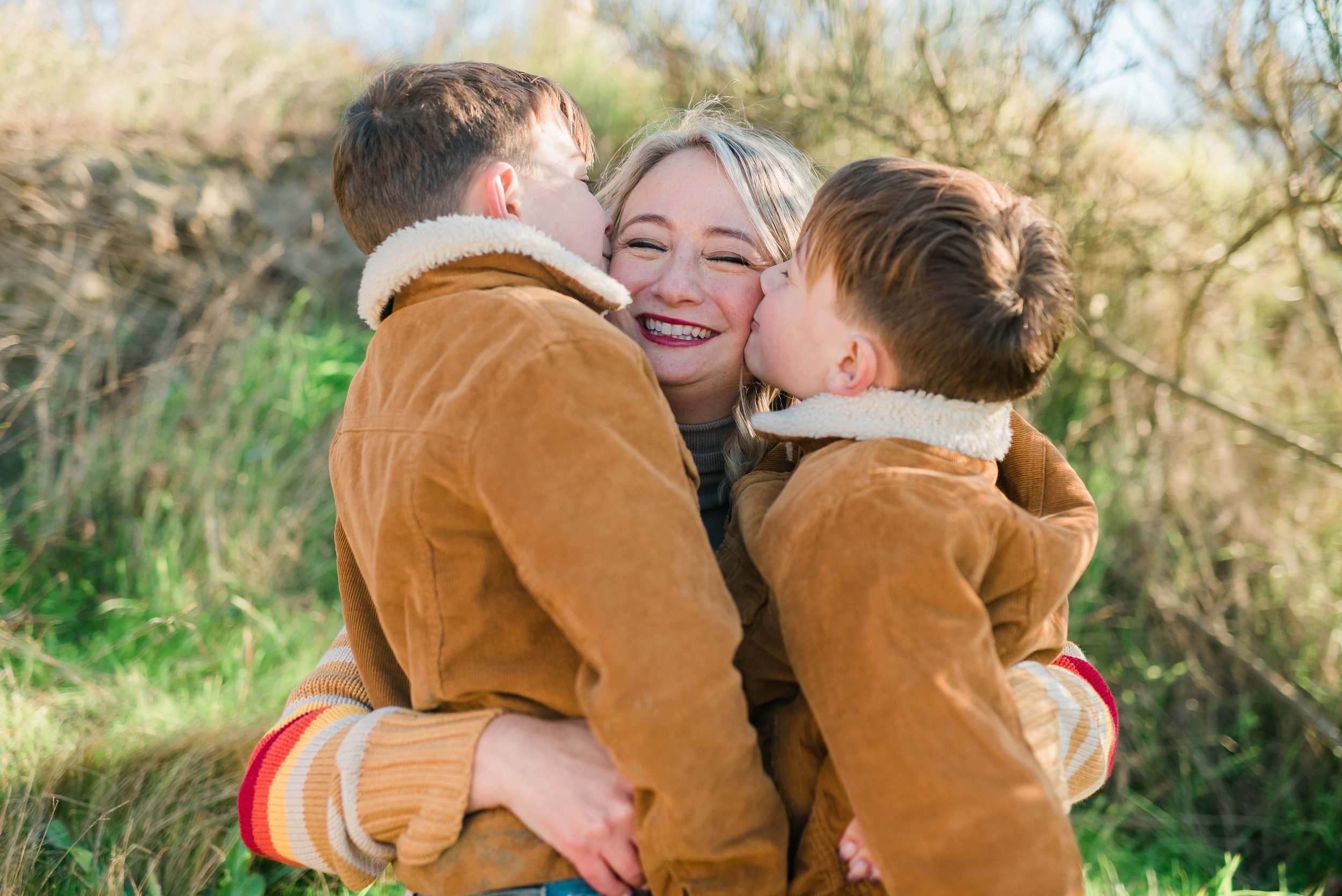  Mom getting kissed on the cheeks by twin sons. 