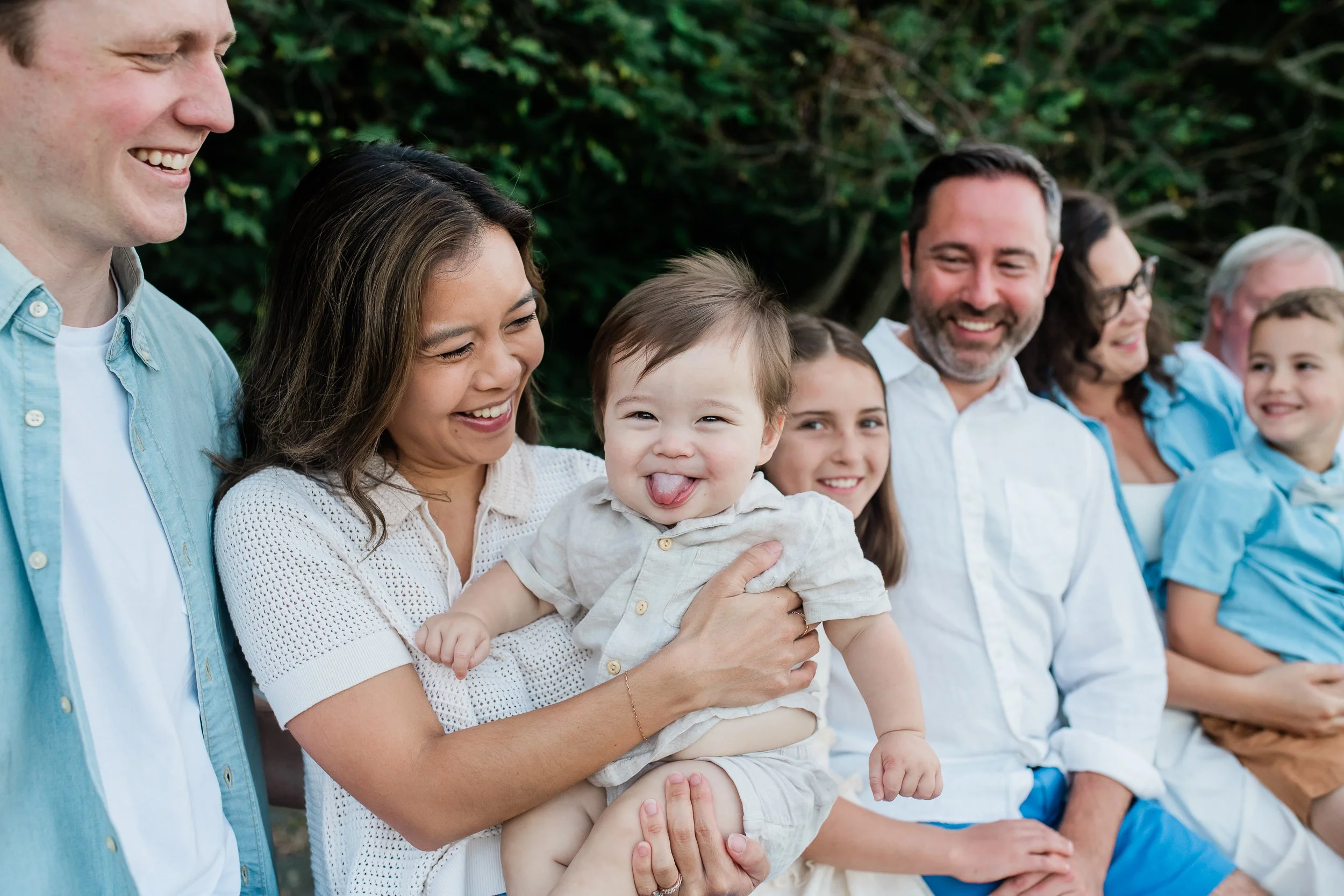 Baby boy sticks out his tongue as parents giggle during an extended family session.