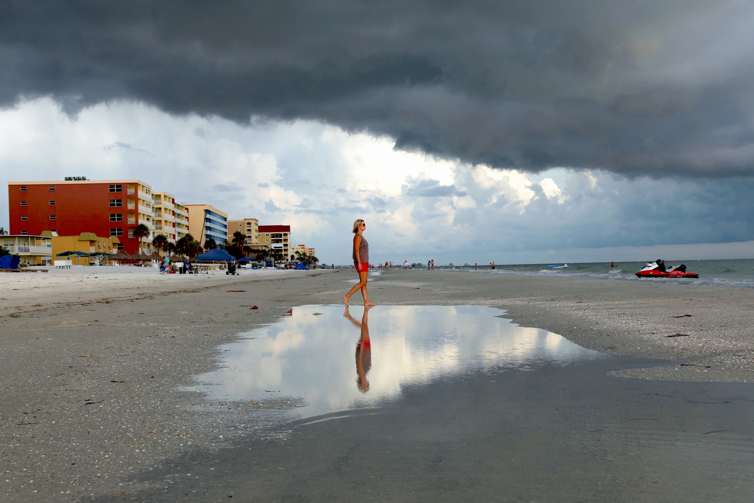  A woman walks towards the ocean as a storm forms overhead. 
