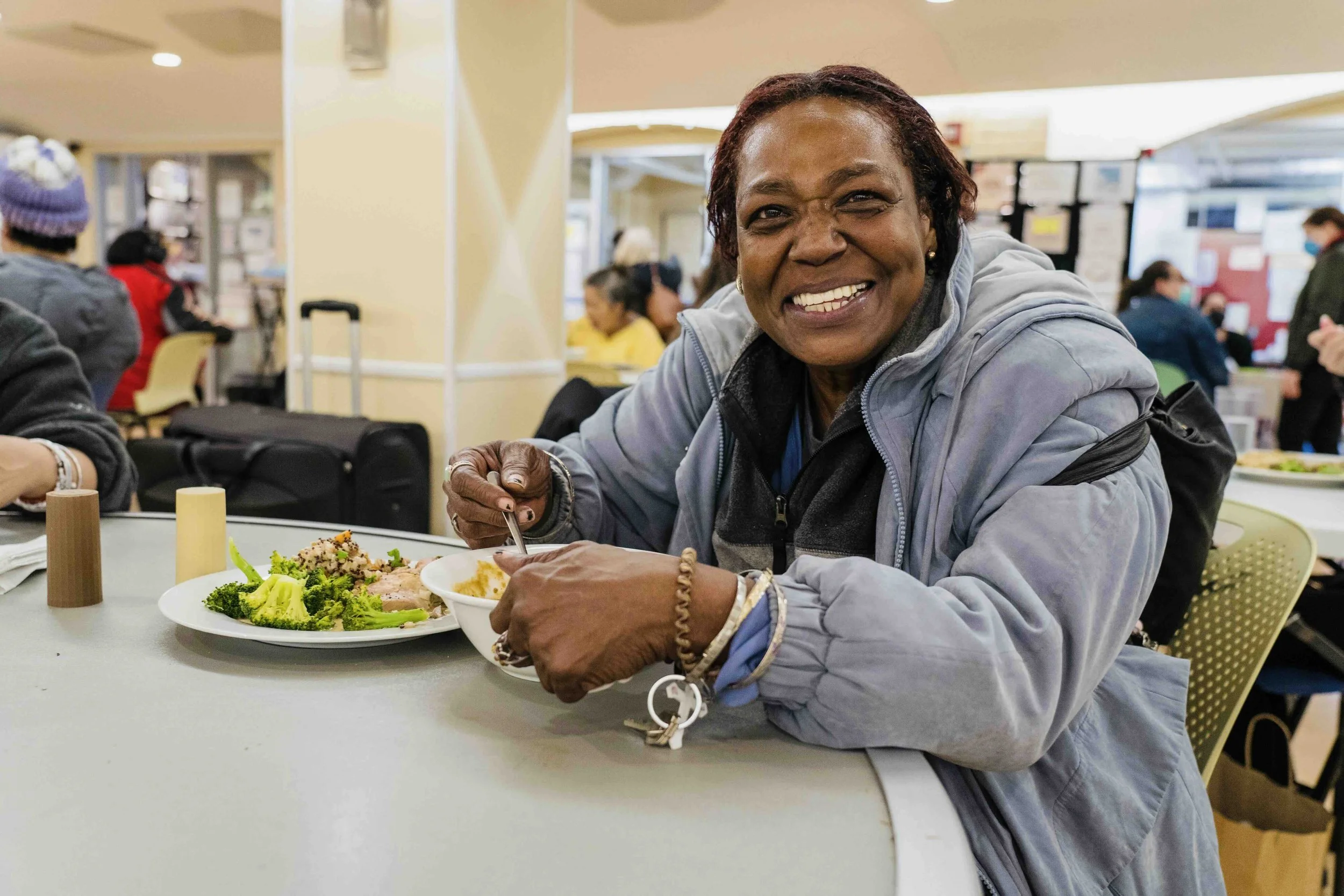 A guest wearing a faded blue jacket enjoys a nutritious meal in the community dining area.