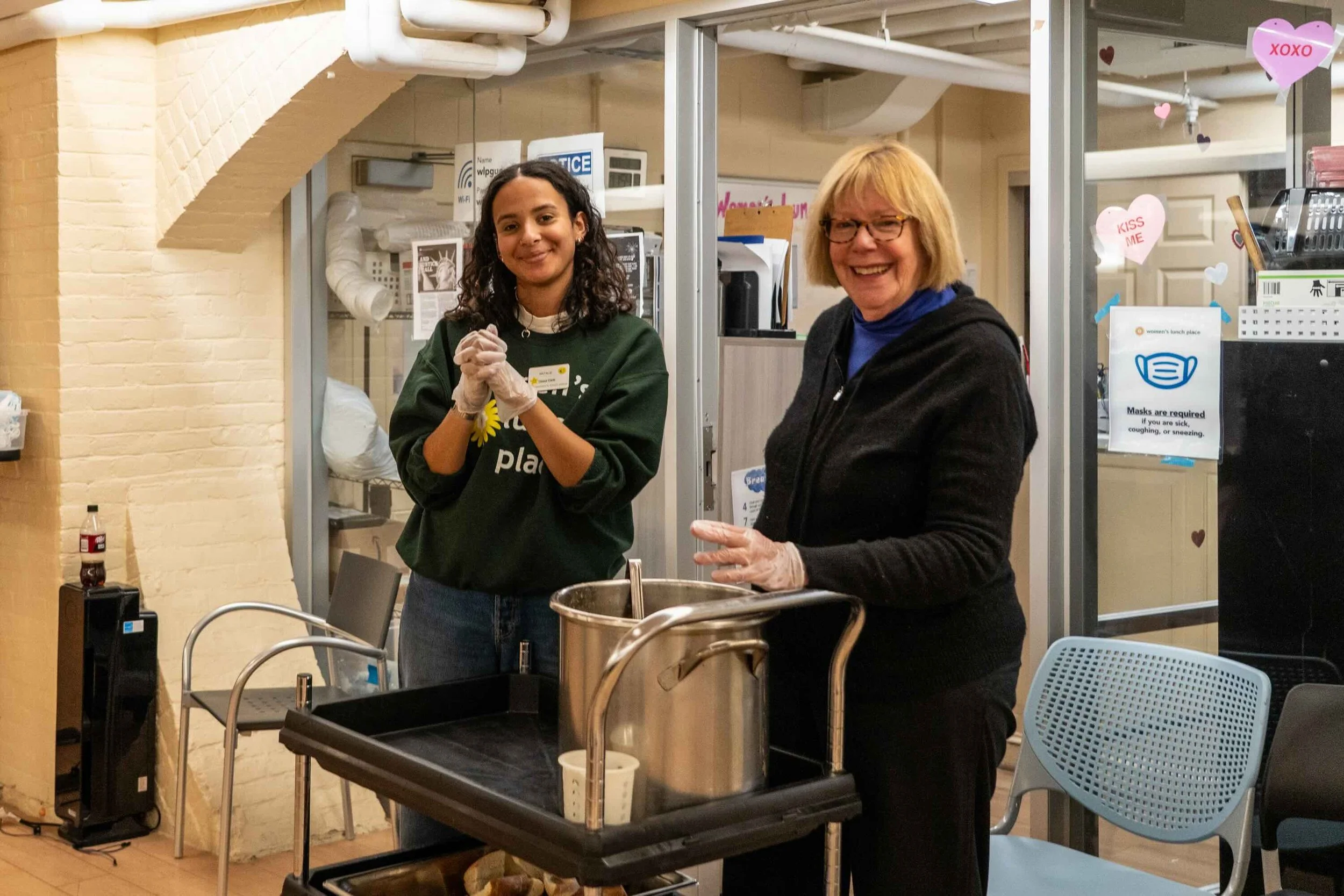 Two volunteers smiling and serving WLP's daily vegetable soup.
