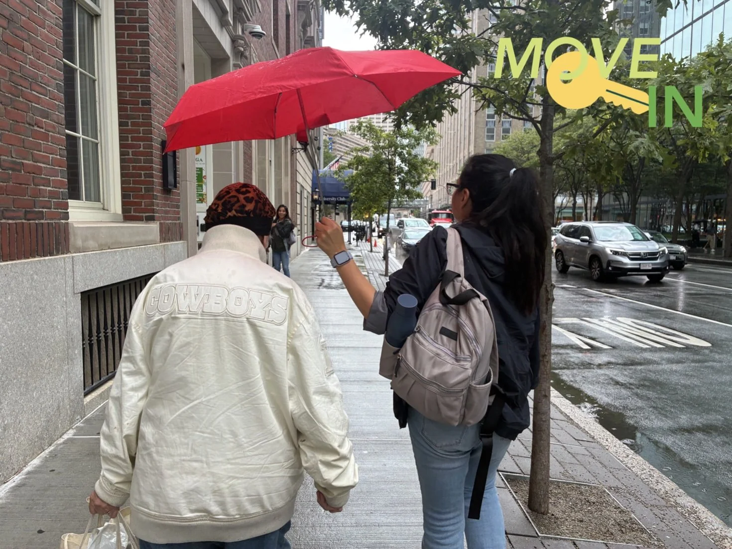 A WLP Advocate holds an umbrella over an elderly guest as they walk down a rainy street.