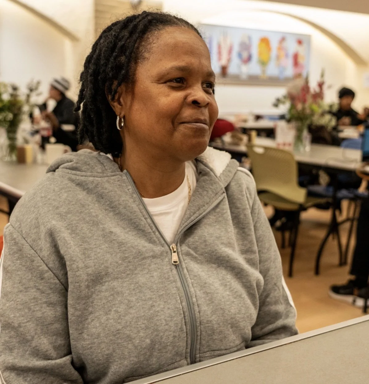 A woman wearing a grey hoodie smiles softly in the dining room of Women's Lunch Place.