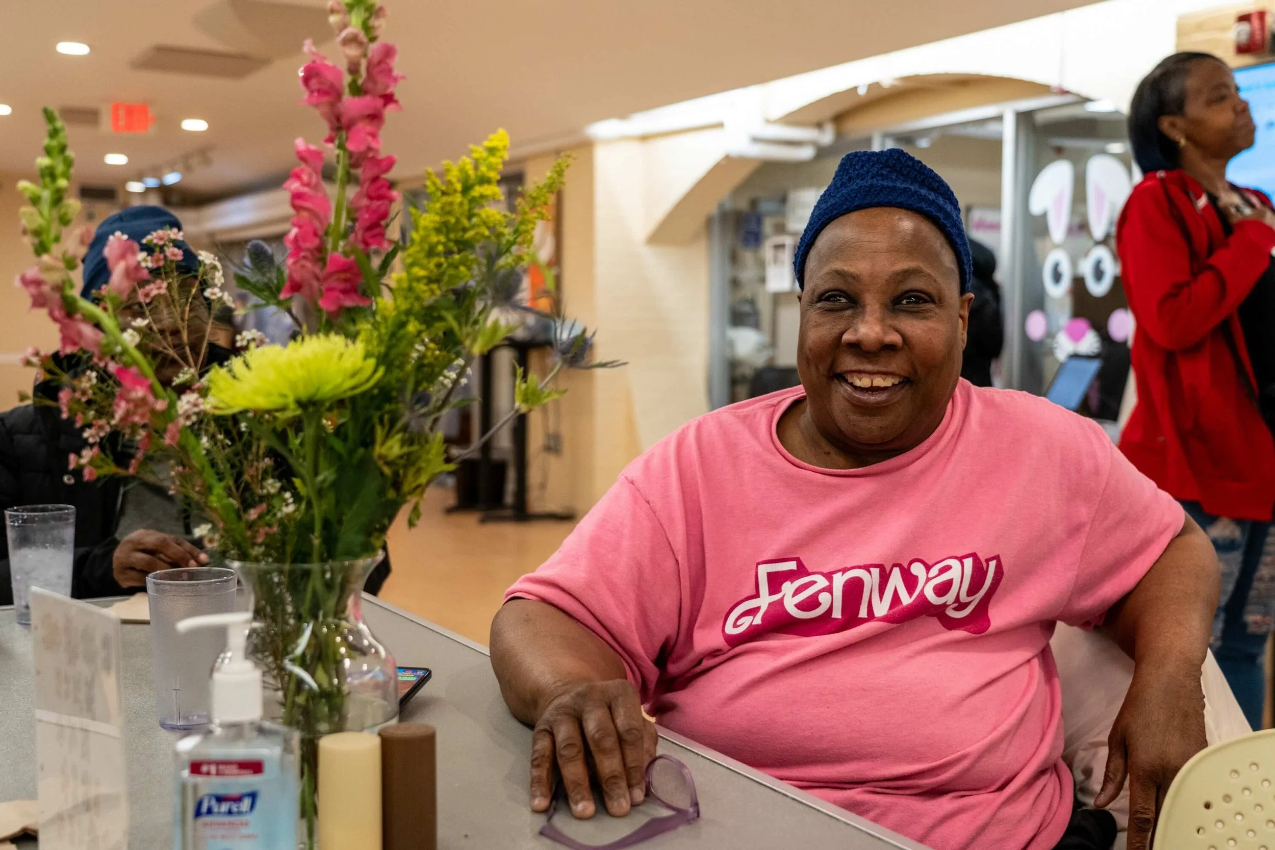 A guest of WLP in a pink shirt smiling at a table adorned with fresh flowers.