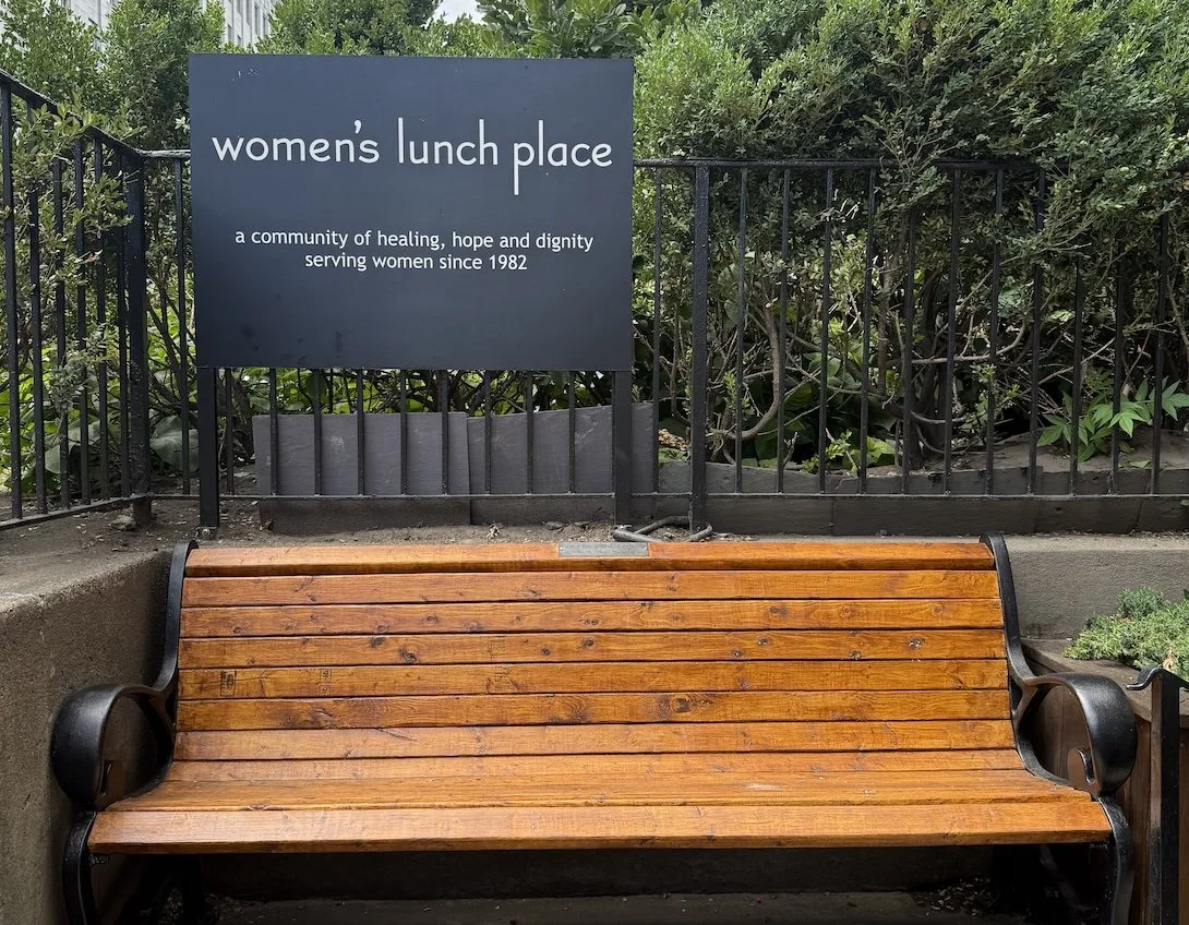 The sign and wooden bench in front of the day shelter at Women's Lunch Place. The sign reads: "a community of healing, hope and dignity serving women since 1982"