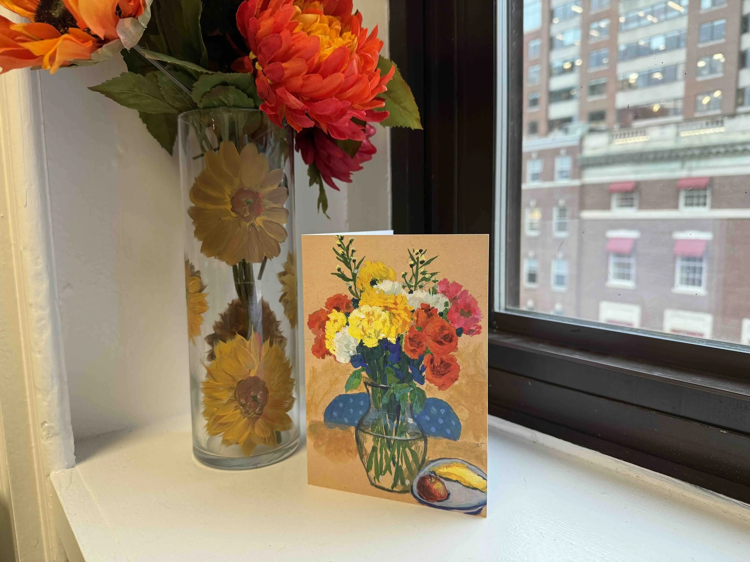 A beautiful Mother's Day card sits on a windowsill next to a vase of flowers.