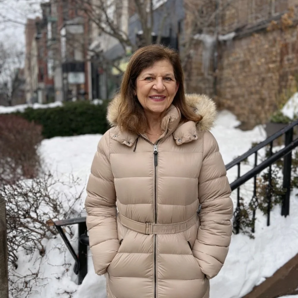 A woman in a winter coat smiles at the camera outside of the day shelter in the snow.