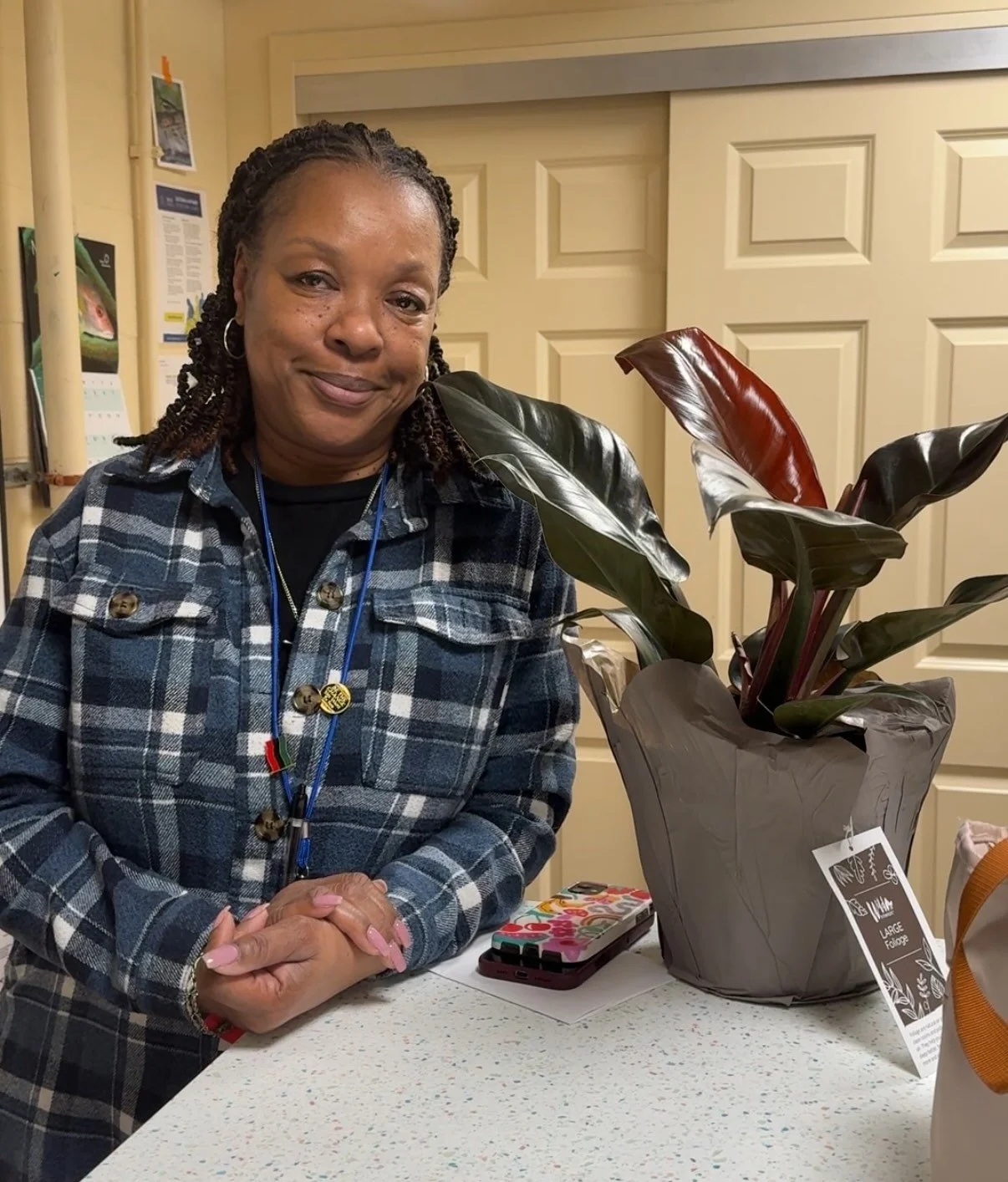 A woman in a plaid shirt stands next to a gift of a beautiful houseplant.