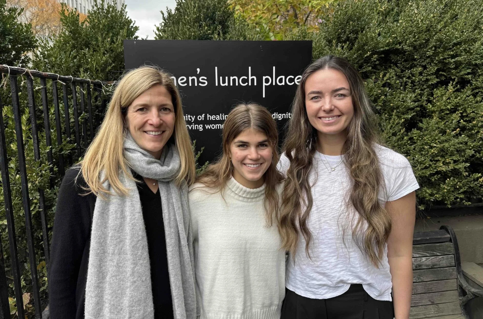 Three women, part of the Marathon team, smiling in front of the Women's Lunch Place sign outside of the day shelter.