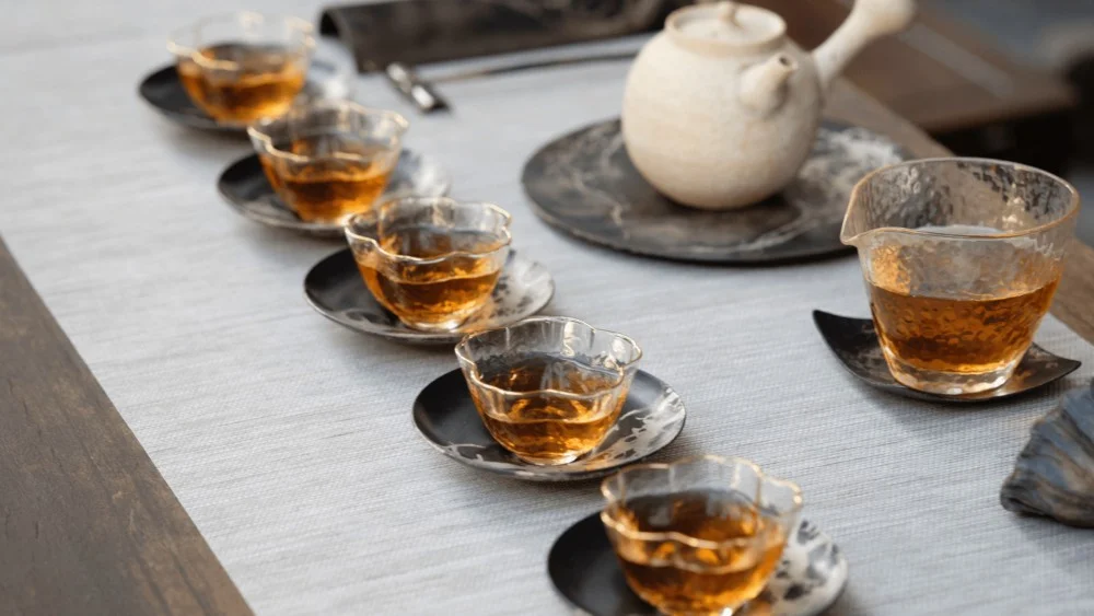 vijf kopjes thee op tafel met een theepot en een glazen kan