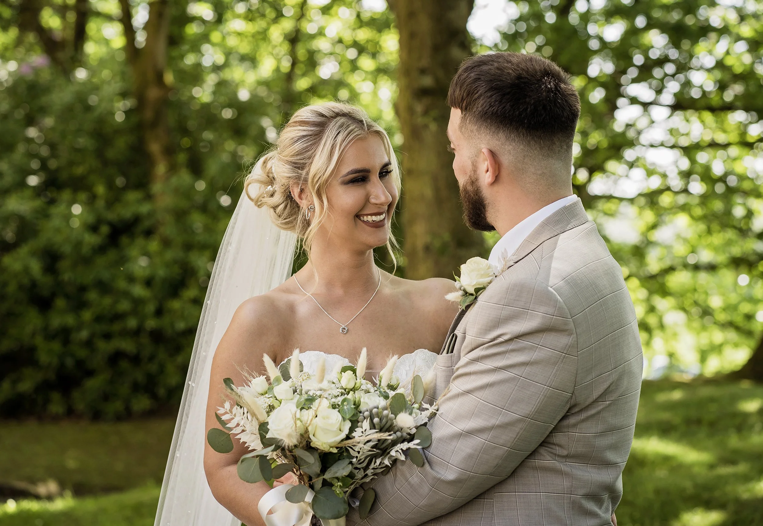 Bride and groom smiling at each other outdoors, bride holding a bouquet of white flowers, at Norton Grange Hotel Rochdale