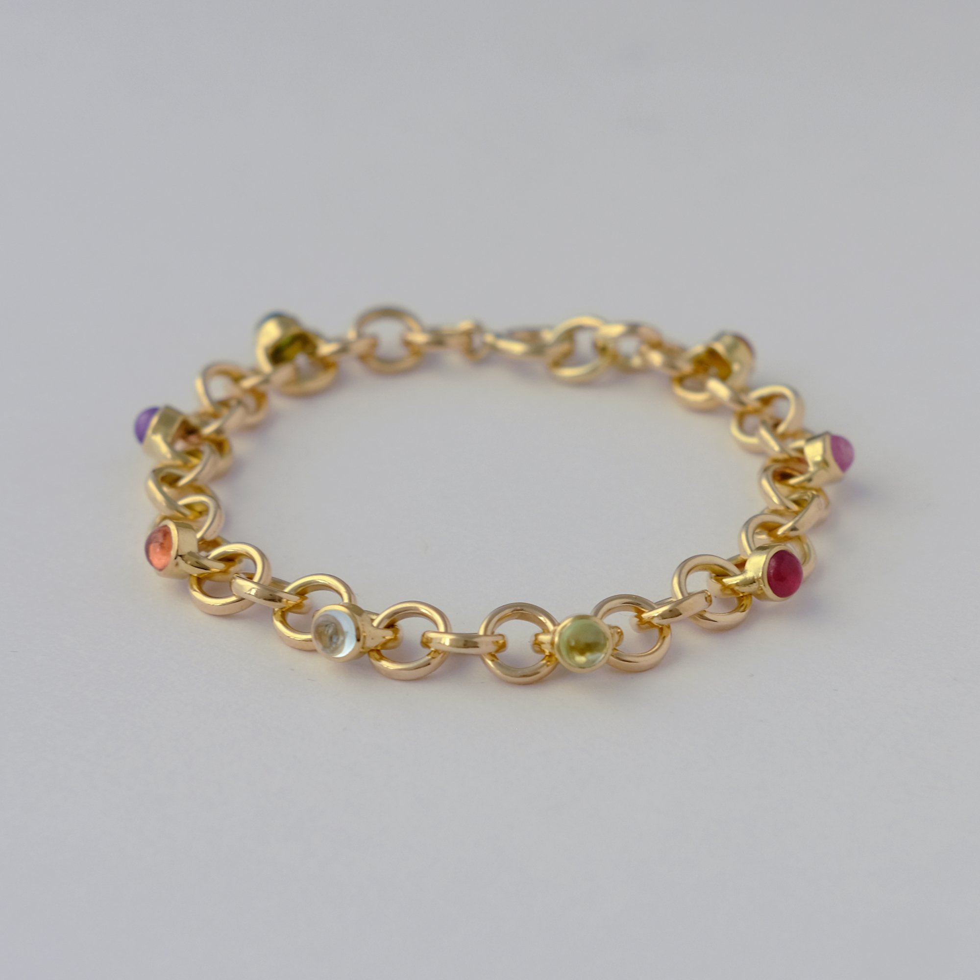 This bespoke gold bracelet is handcrafted by a goldsmith and set with many differently coloured gemstones. A luxury gold gemstone bracelet combining fine craftsmanship, vibrant precious stones, and custom design.