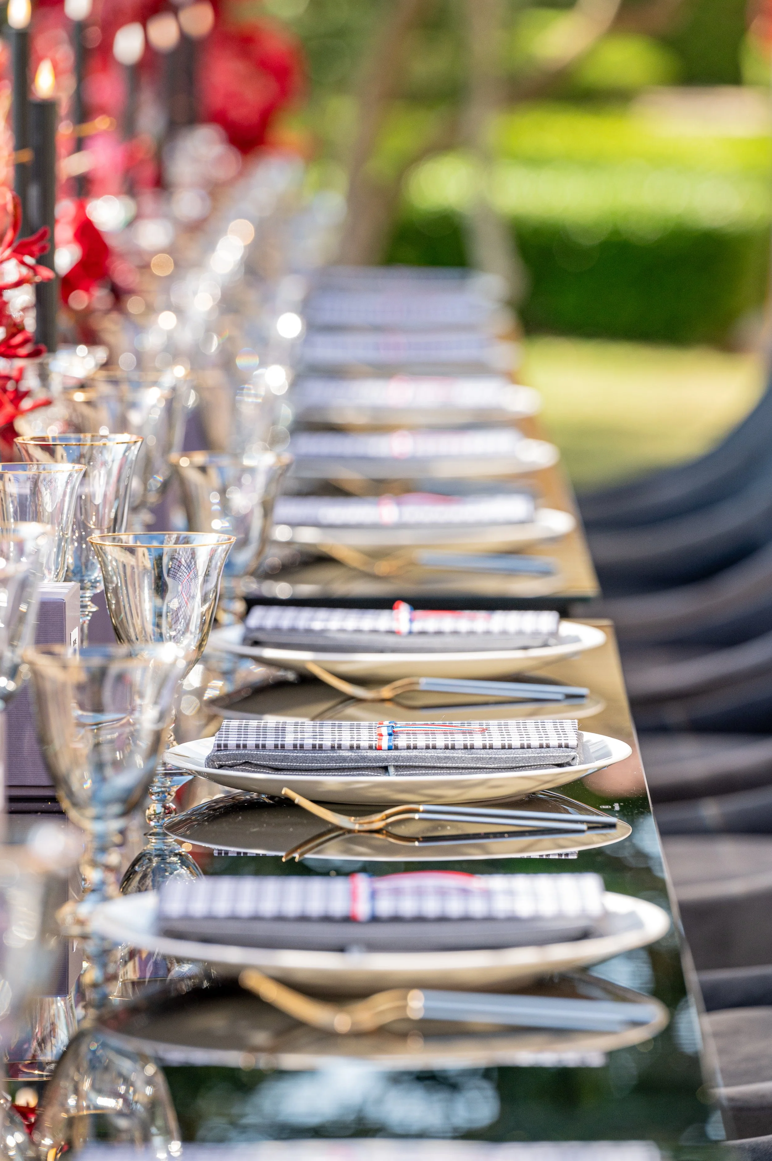 Elegant outdoor dining table set with plates, glasses, and napkins, arranged for a formal meal with a garden in the background.