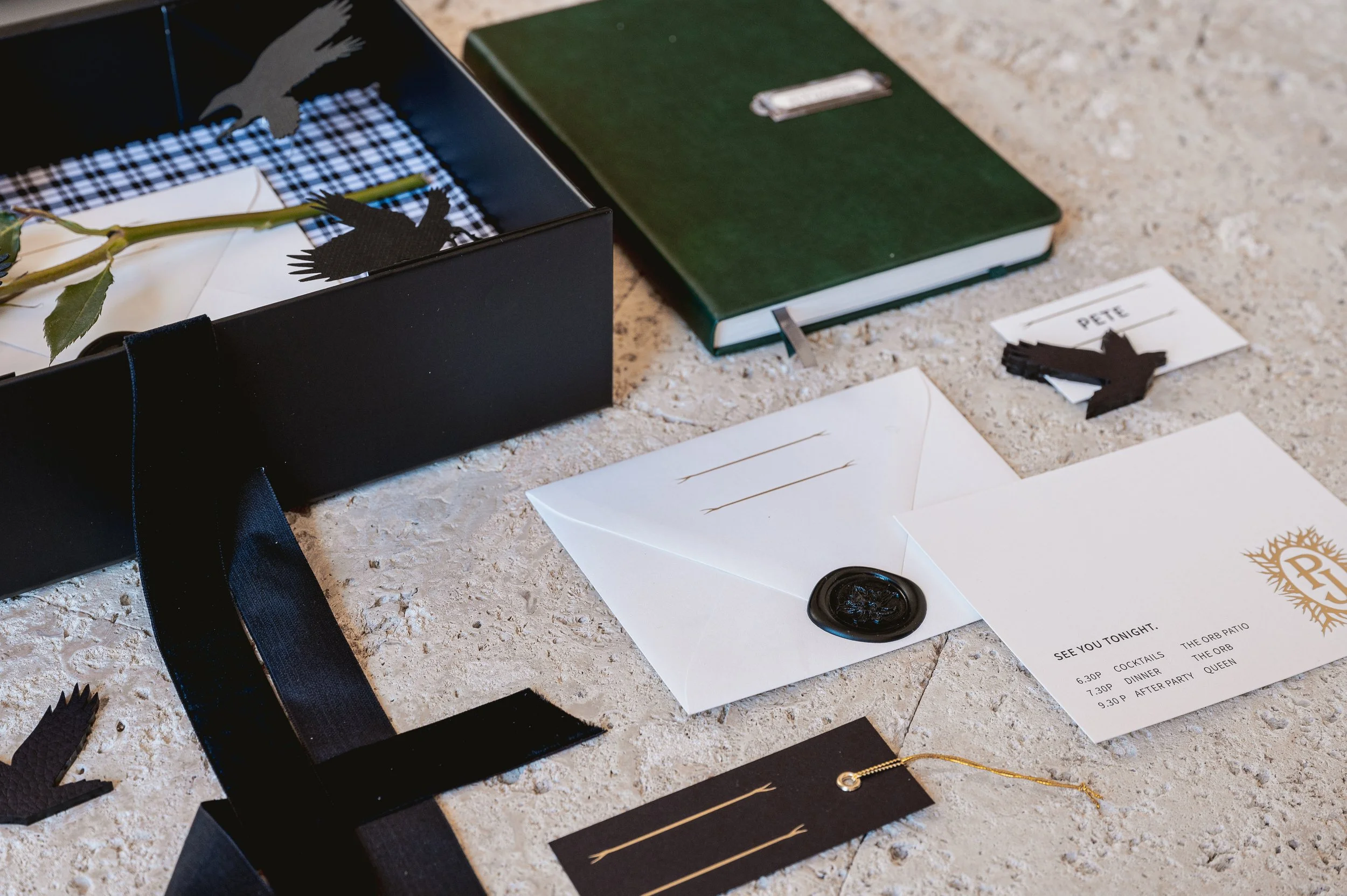 Letter, envelope, and decorations on a stone surface, with a black gift box, green notebook, and paper cutout of a bird.