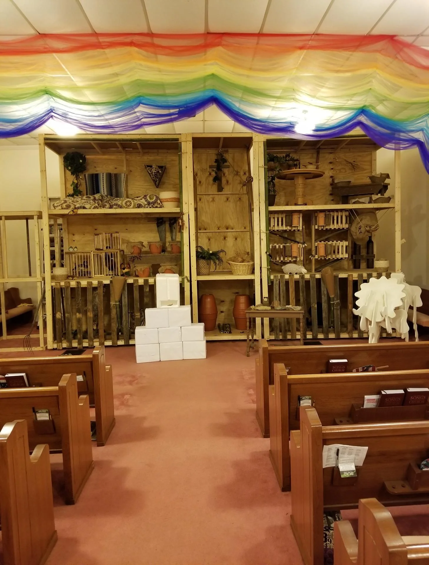 This is a fantastic view of our VBS and the model ark we built to replicate key necessities for Noah, his family, and the animals to live through the global flood. Here you see the culmination of all nights: (1) building the ark, (2) the flood and taking care of the animals, (3) stepping off the ark, the rainbow, and the altar (not shown), (4) the evidence today which supports the occurrence of a global flood. Quick Overview: The Ark: (Bottom Deck) Large animal cages (complete with stuffed animals); one cage was used in VBS for kids playing the role of animals, dressed in costumes, being fed by Noah; this was a great photo opportunity for all! (Second Deck) Containment for birds, reptiles, amphibians, small animals, and food storage. (Upper Deck) Living quarters and a kitchen for Noah and his family. Our model also included features such as water containment and disbursement, air flow, and manure cleanup. The Rainbow: (Top of Picture) The rainbow represents God’s covenant with man to never again flood the earth with water. God is trustworthy to keep His promises! Evidence of a Global Flood: (Foreground Exhibits) Dinosaur Fossils: how rapid sedimentation forms fossils, and what this reveals about dinosaurs’s co-existence with man; Invertebrate Fossils: why are seashells found all over the world and on the highest mountains? The Lost Squadron diorama: how ice rings counted from The Lost Squadron rescue operation prove evolutionary dating for the world is wrong. We used all these evidences to analyze modern evolutionary information taught in public schools, and compared these teachings to long-withstanding scripture, recorded in the Bible. Special thanks to our members who built and/or contributed each item seen in this picture. We also thank the Ark Encounter in Kentucky for supplying our minds with knowledge and ideas which planted our hearts, rooted our design, and grew our faith.