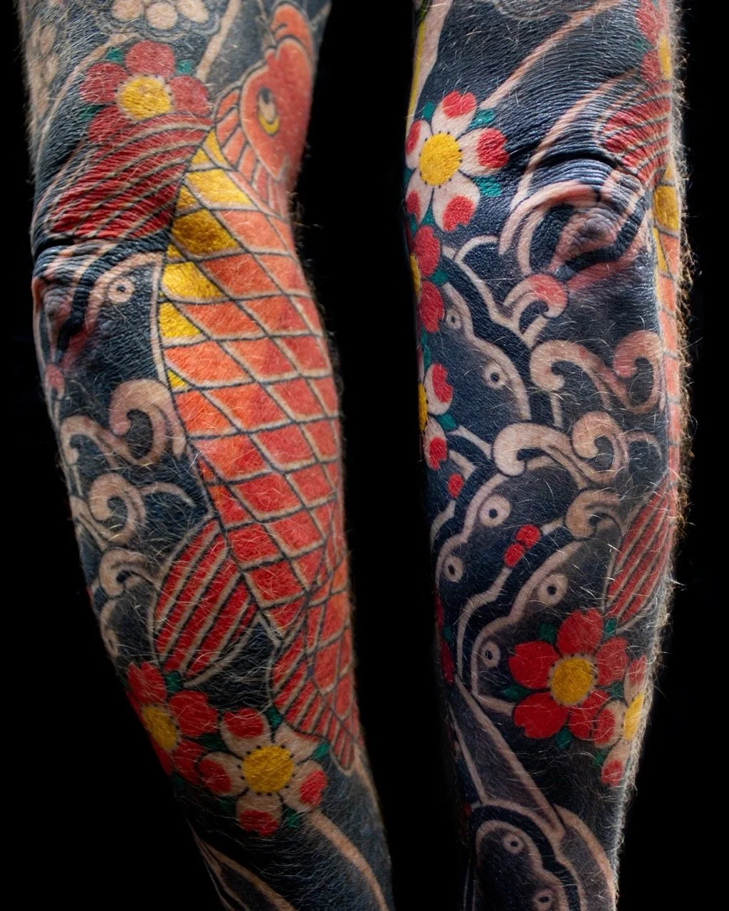 Close-up of traditional Japanese irezumi sleeve details showing a red koi fish, light grey waves, dark water bars and colourful sakura flowers.