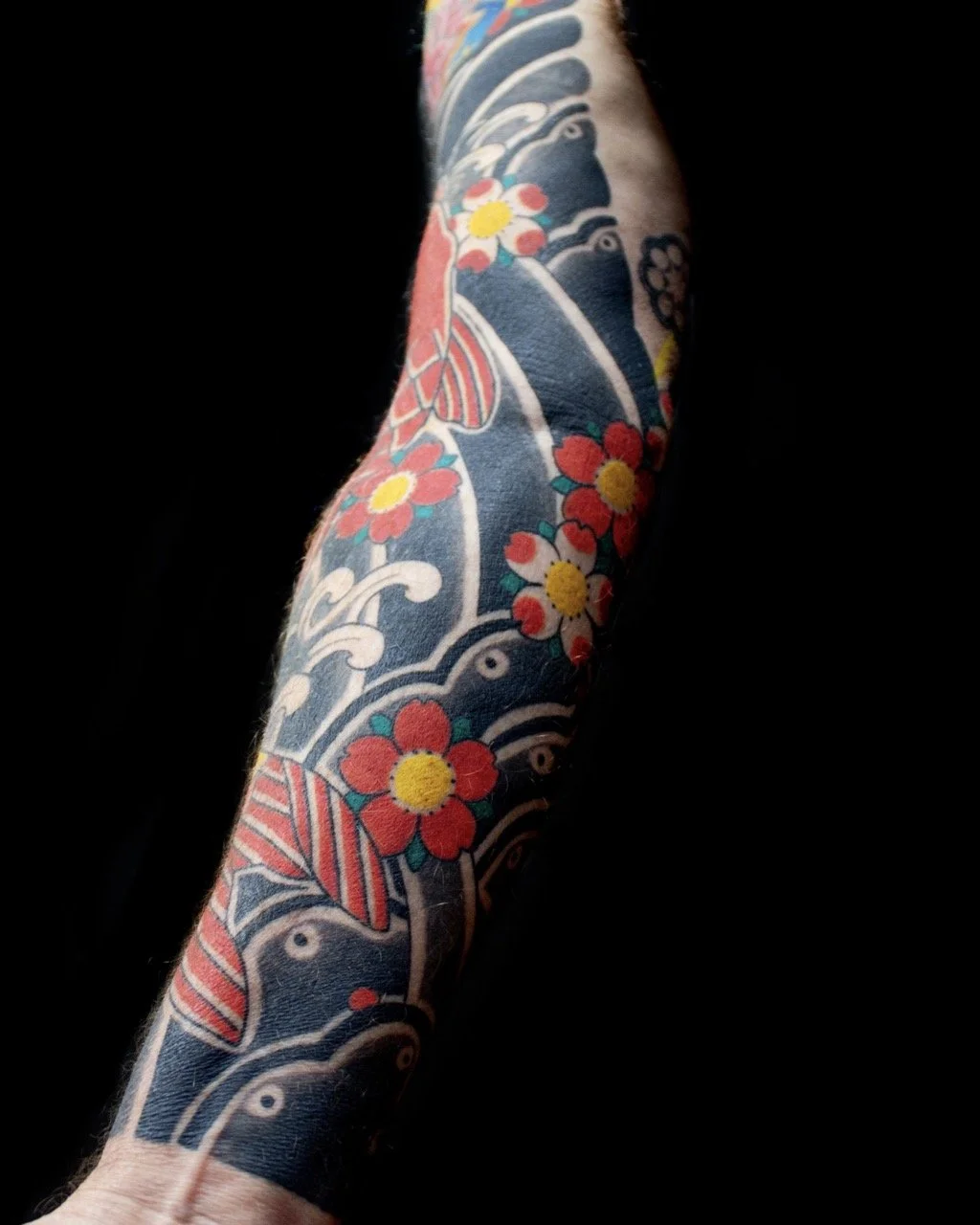 Traditional Japanese irezumi sleeve featuring dark blue water bars, light grey waves, red and white sakura flowers and red koi details.