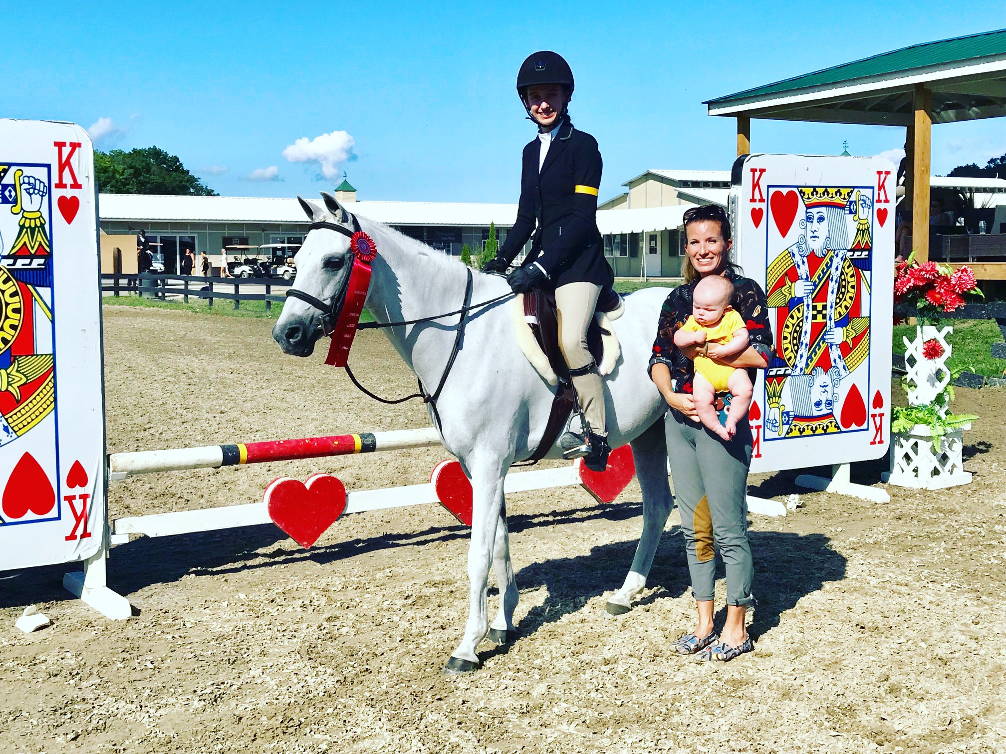 Gray pony and girl receiving awards in the show ring from a woman with a baby in her arms