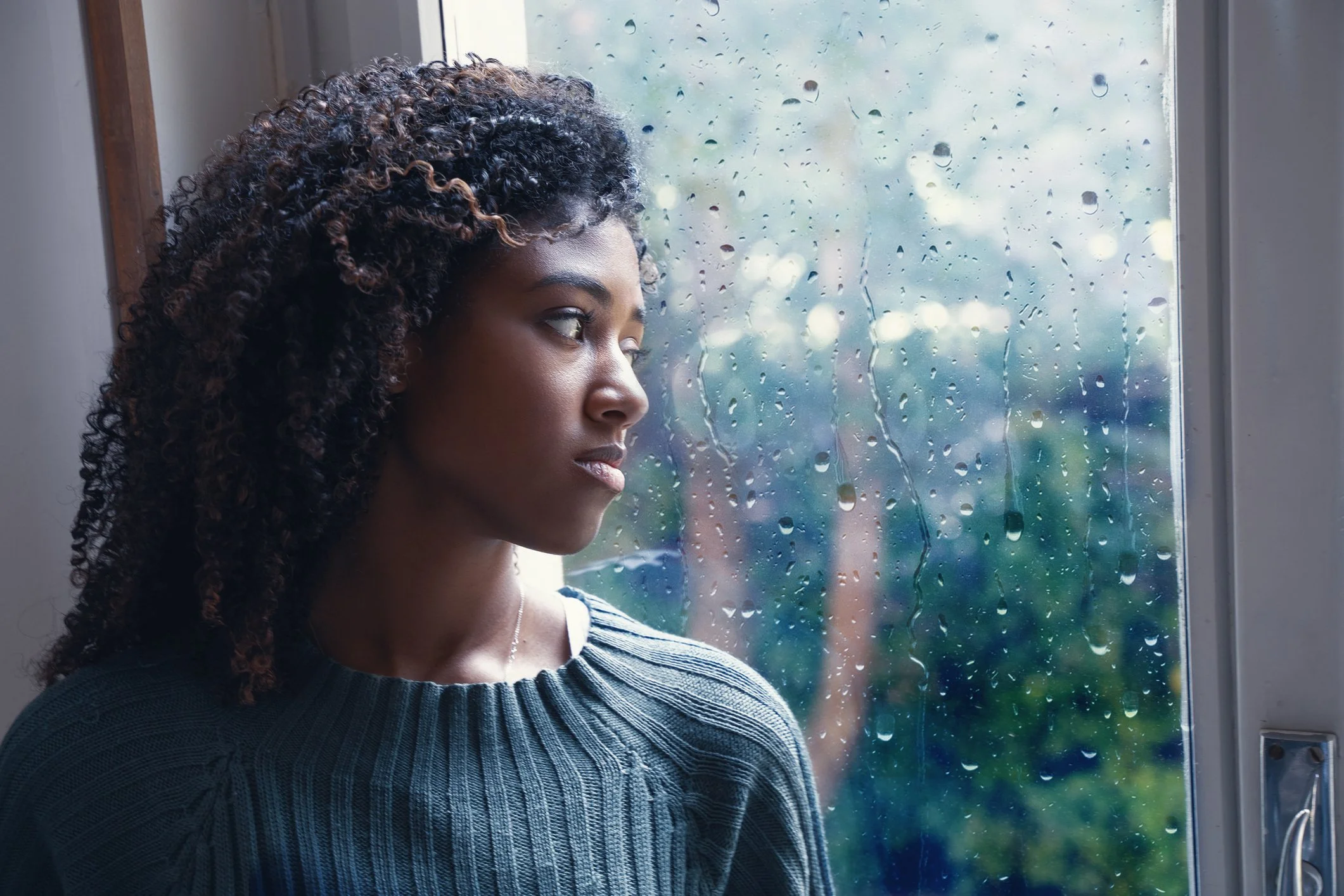 black woman looking out rainy window | woman with anxiety | woman with depression | women and seasonal affective disorder | therapy in Wilmington, NC