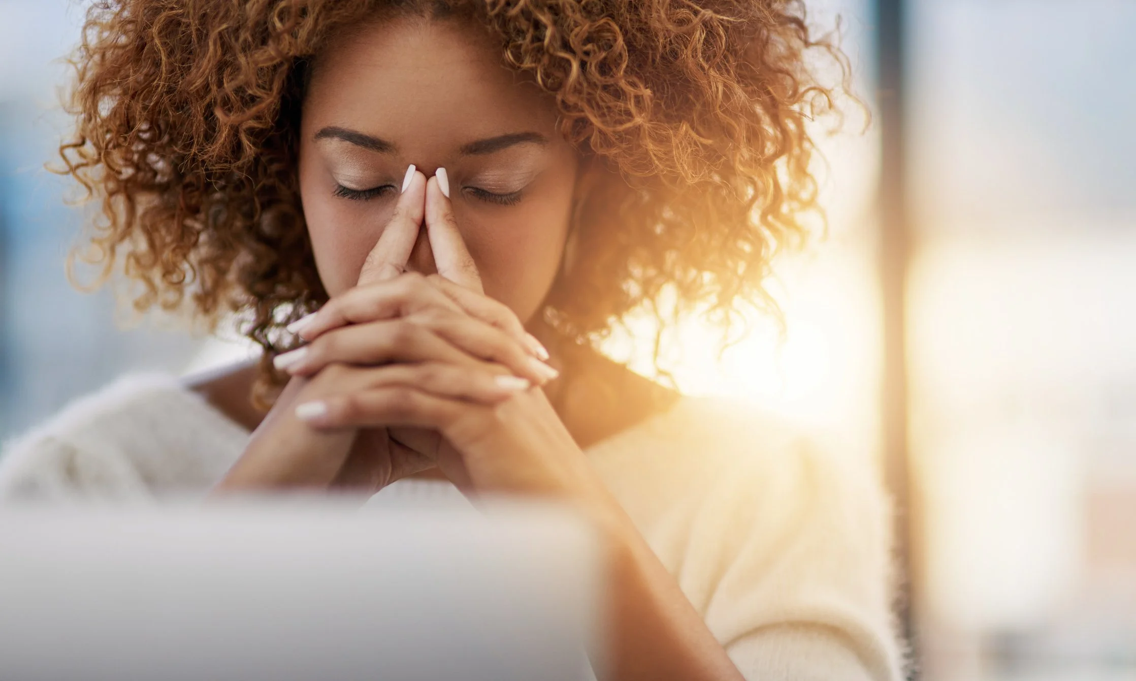 Black woman sitting at laptop with eyes closed and her hands on her face from burnout.