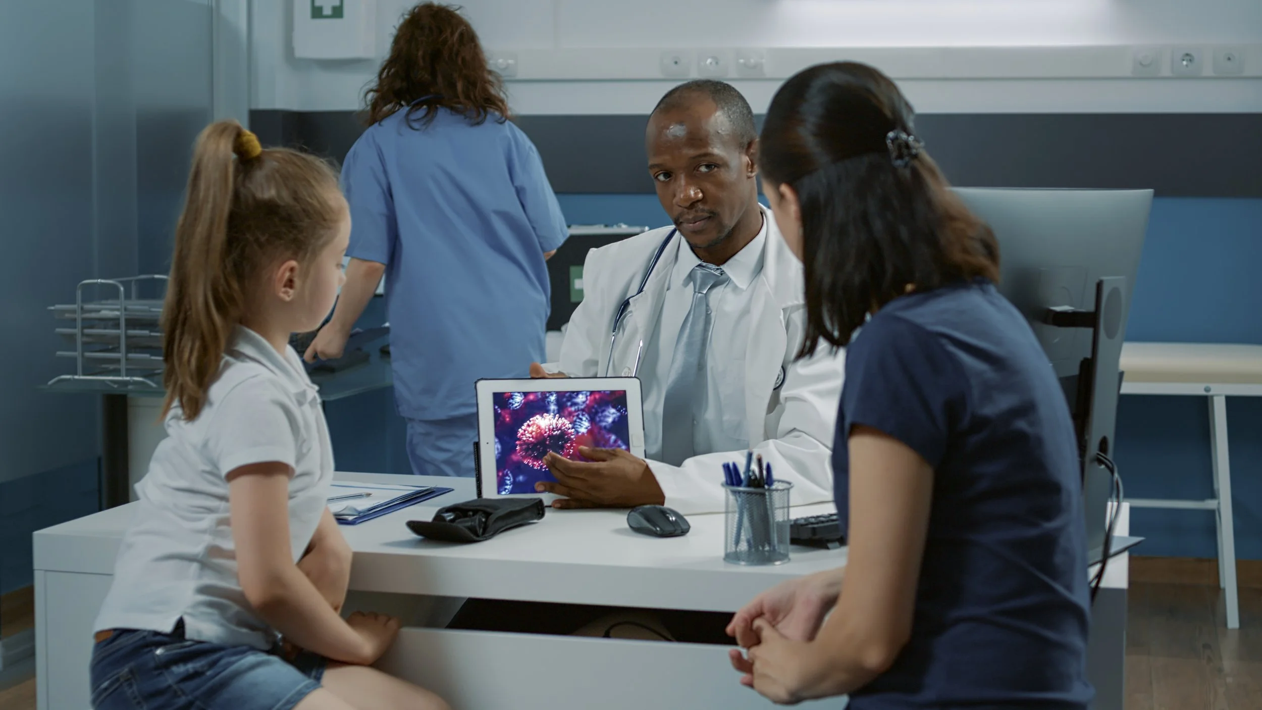 Doctor showing a tablet with fireworks display to young girl and woman in a hospital room.