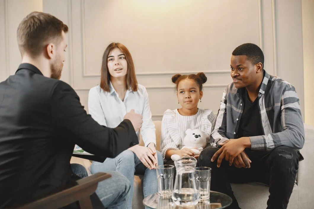A diverse group of four people engaged in a conversation in a living room, with glasses of water on a table in front of them.
