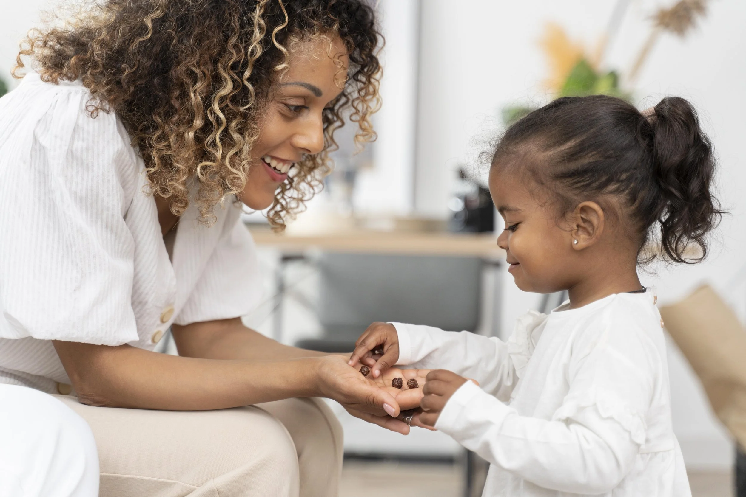 A woman and a young girl exchanging chocolate truffles in a bright, modern office setting.