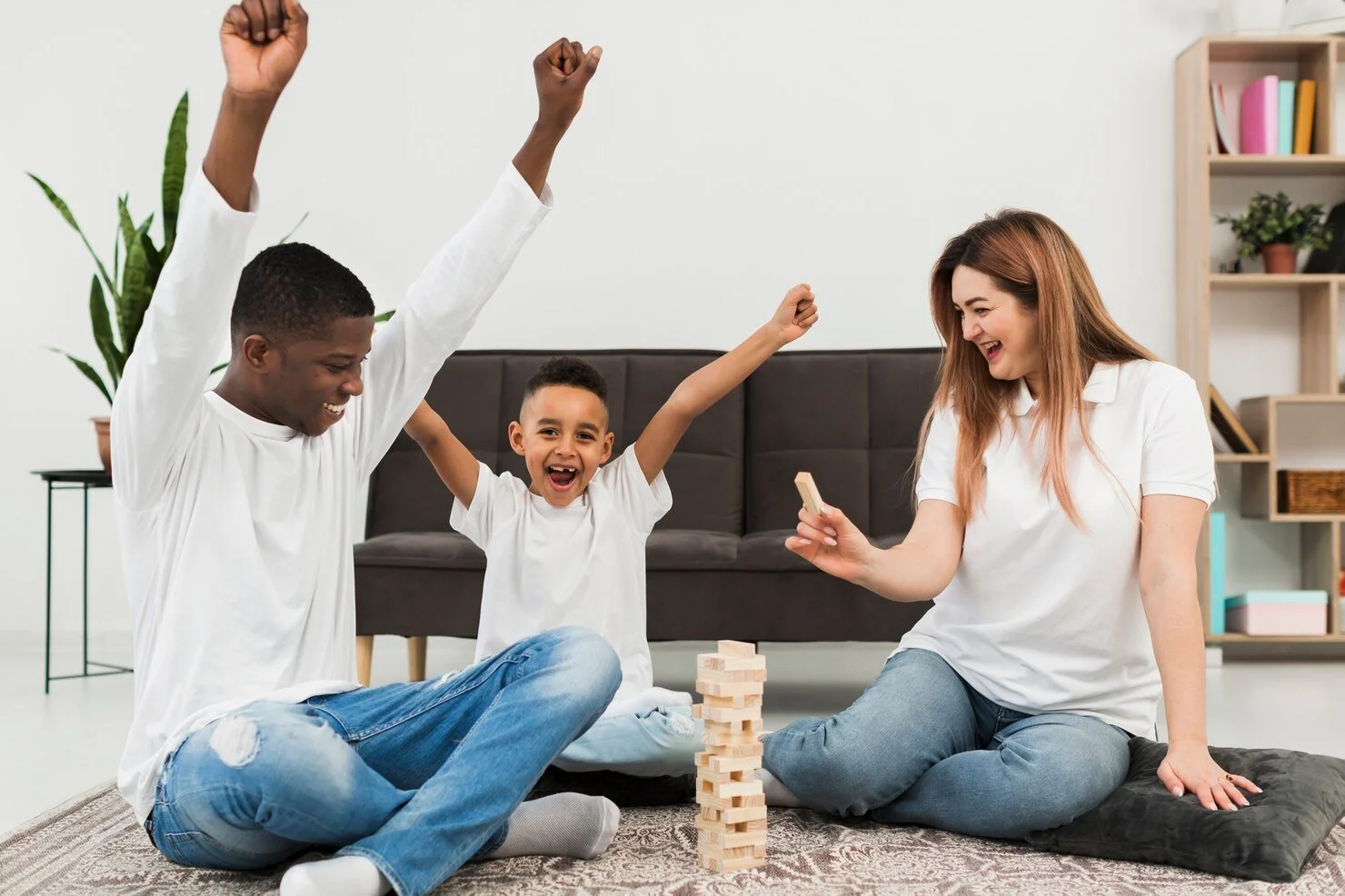 A family playing Jenga on the floor, with two children and a woman, all smiling and celebrating.