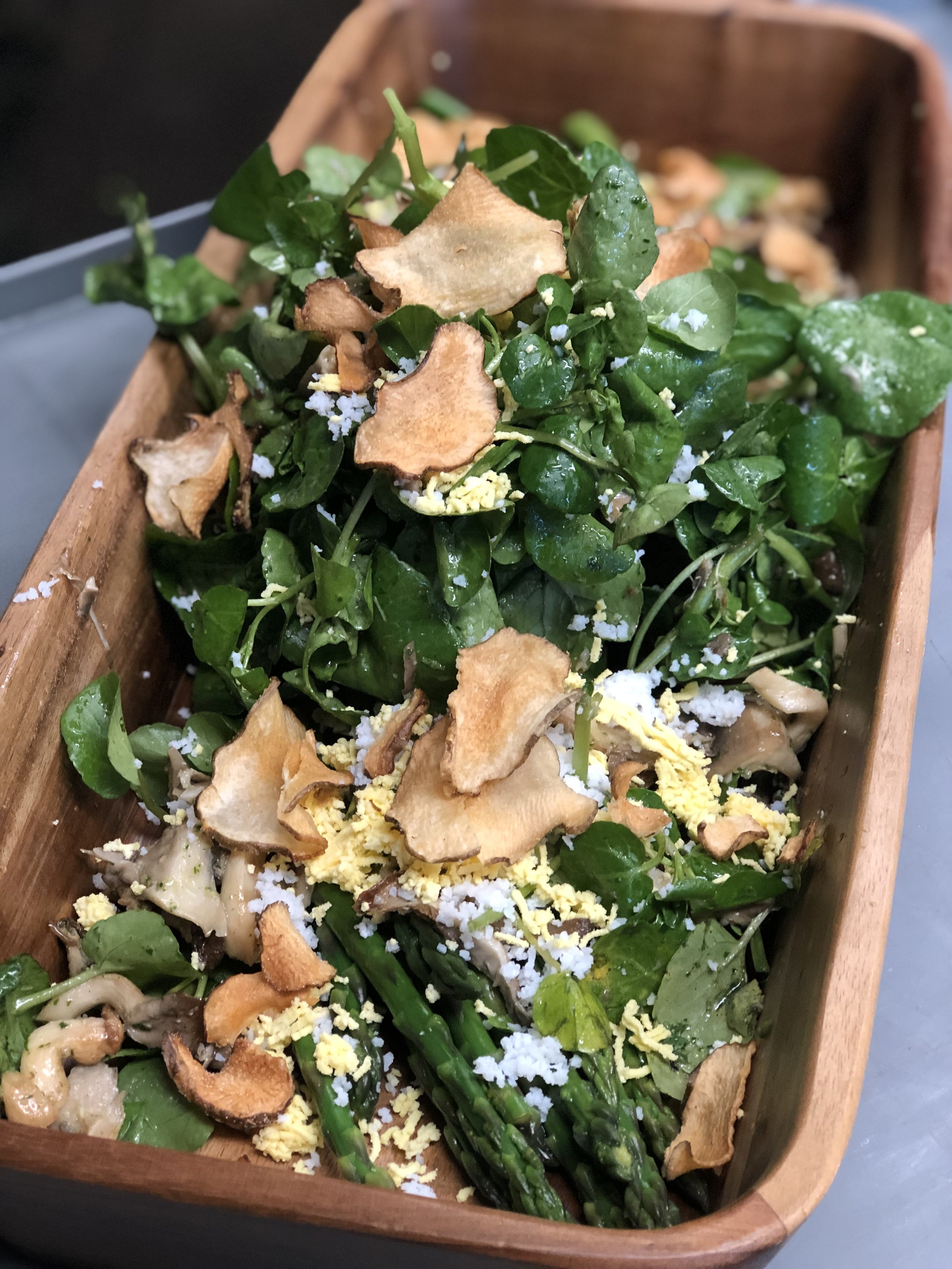 Fresh green salad with cooked mushrooms, shredded cheese, and crispy vegetable chips in a wooden bowl.
