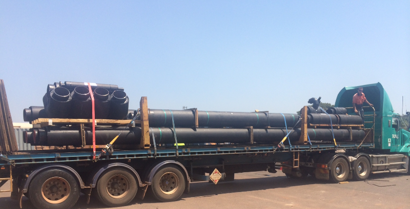 Truck carrying large black pipes