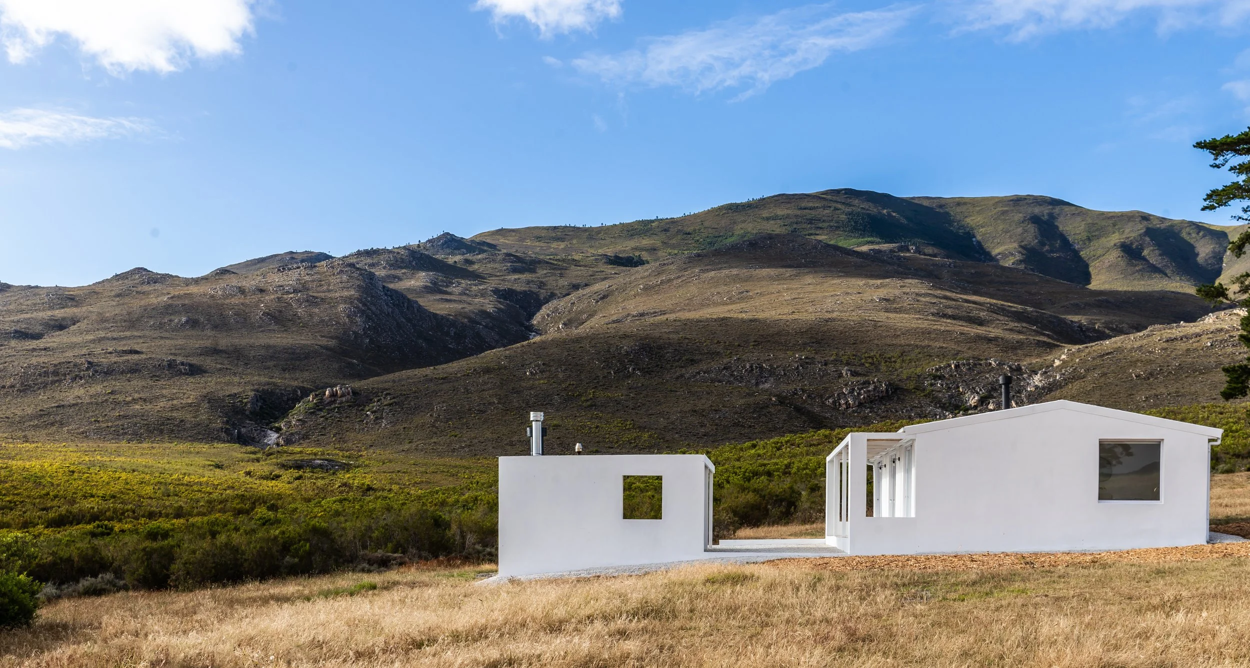 White modern house set against a mountain backdrop with blue sky and grassy landscape.