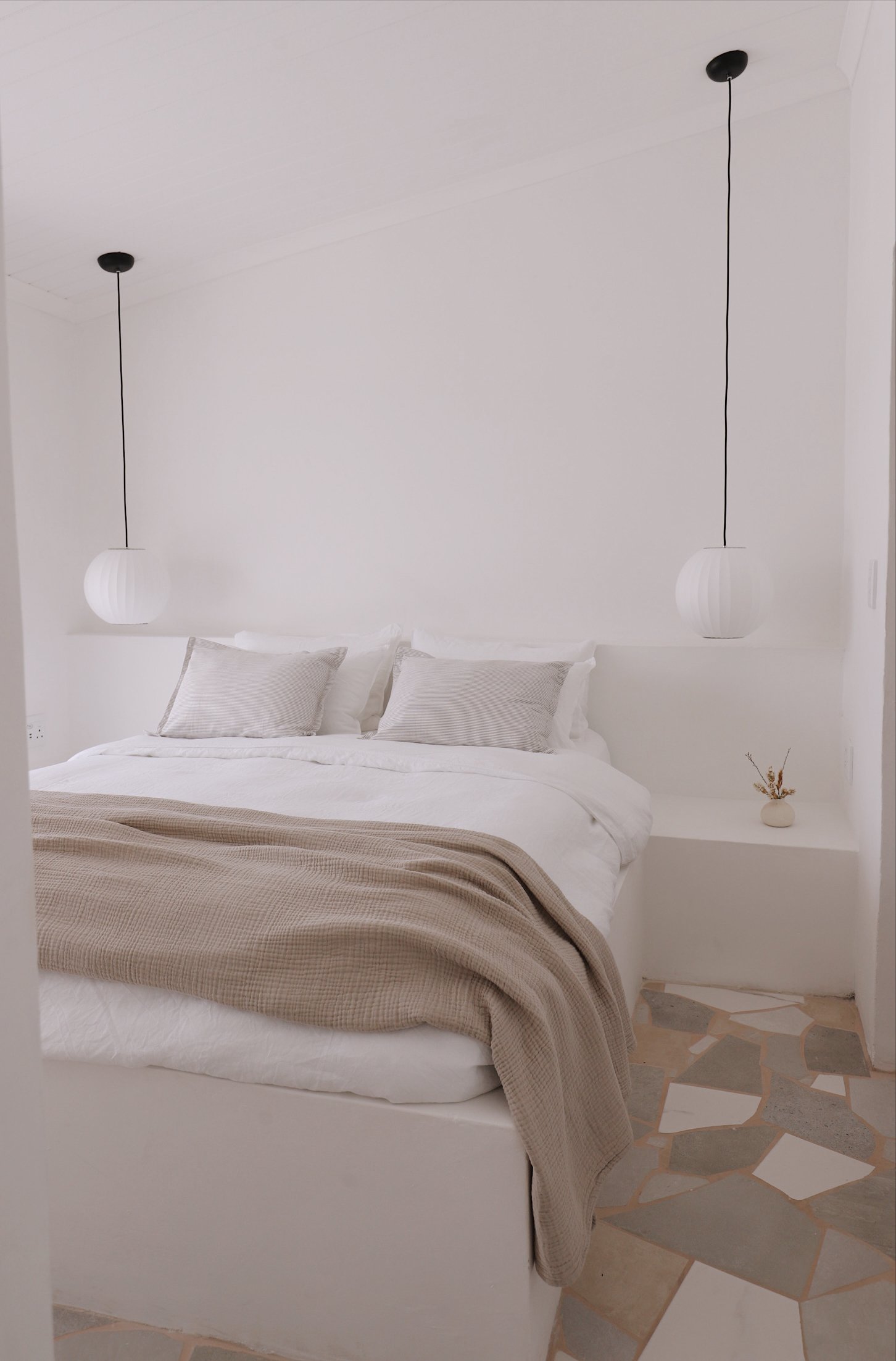 Minimalist bedroom with white bedding, beige throw, pendant lights, and geometric floor tiles.