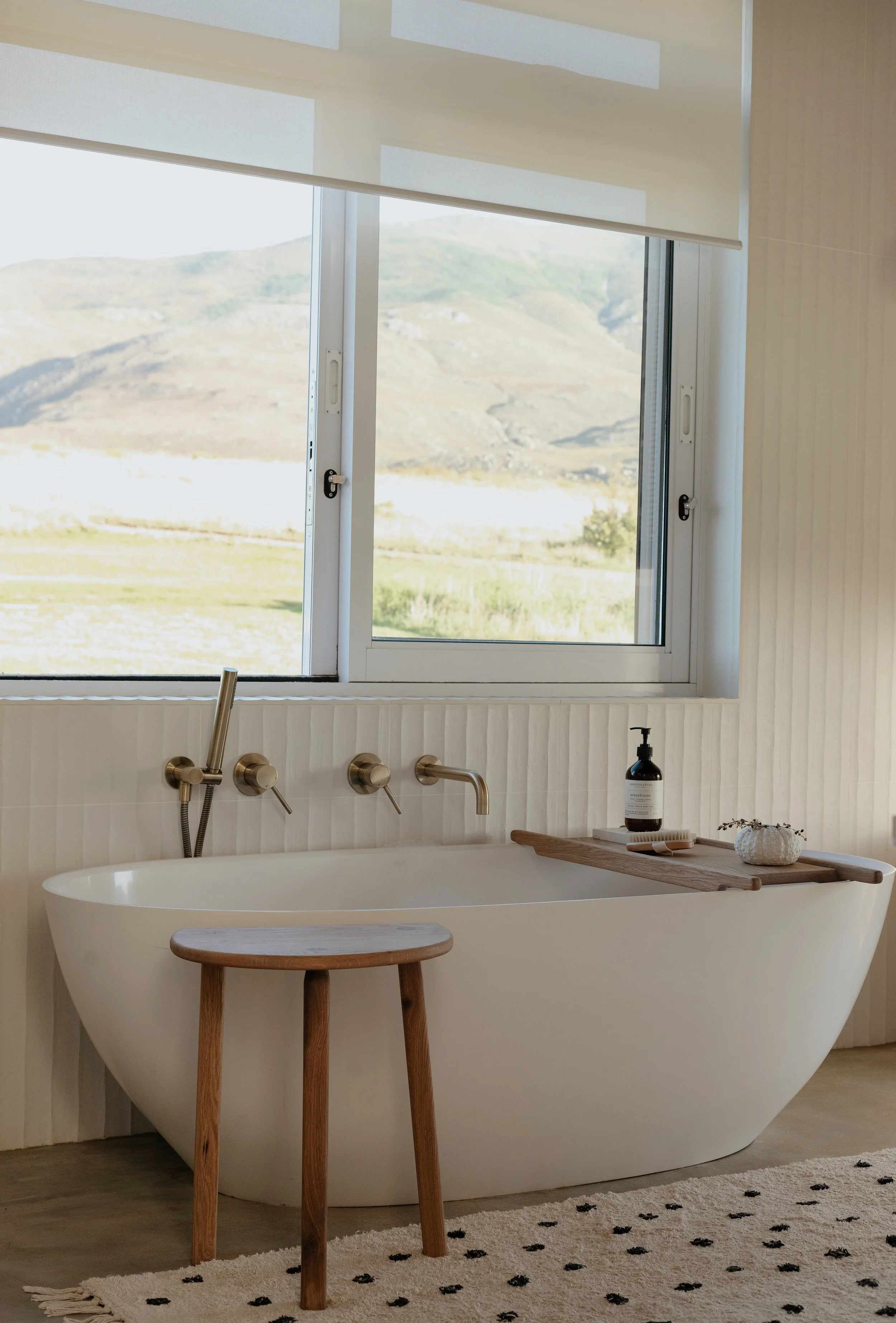 Freestanding bathtub with wooden stool and bath caddy in modern bathroom with large window