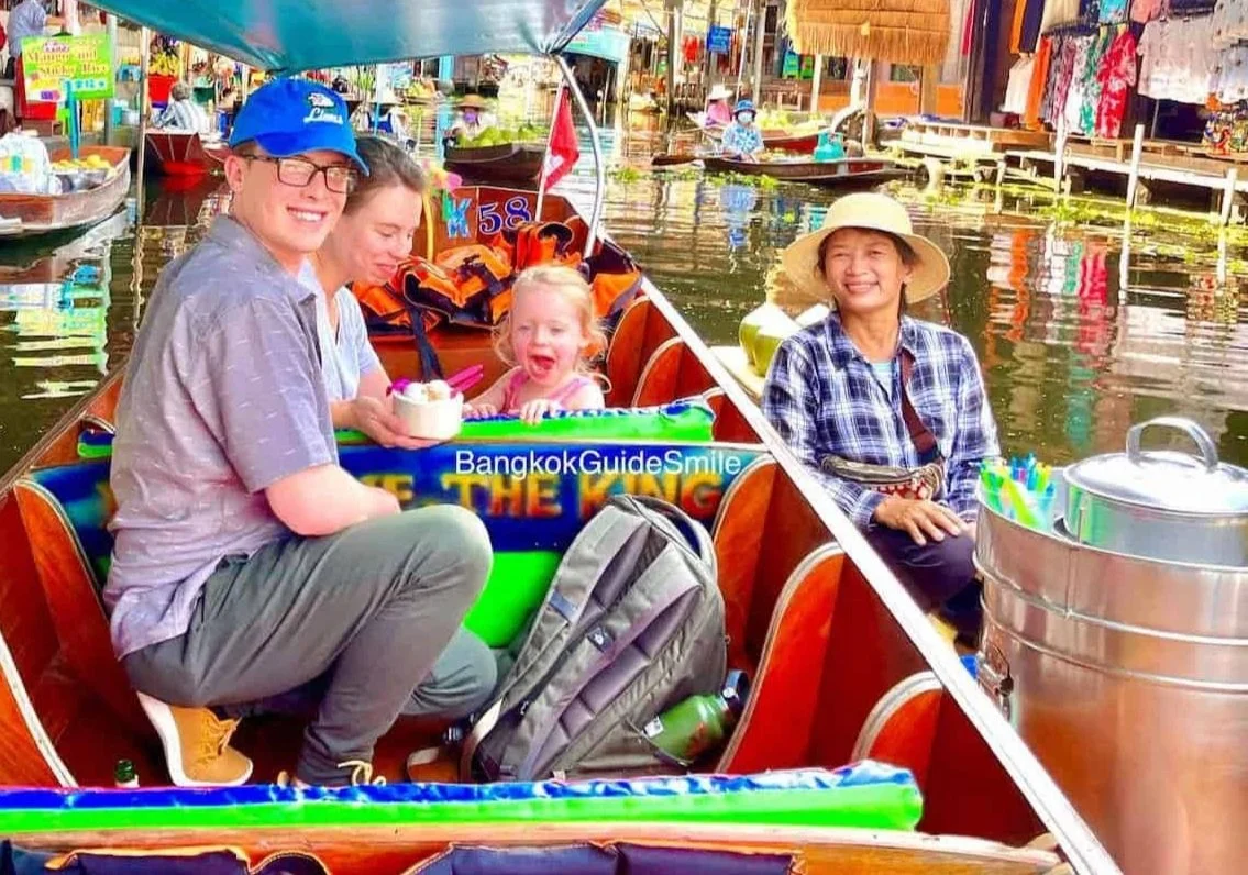 People enjoying a boat ride on a canal market in Bangkok, Thailand, with colorful stalls and water reflections.