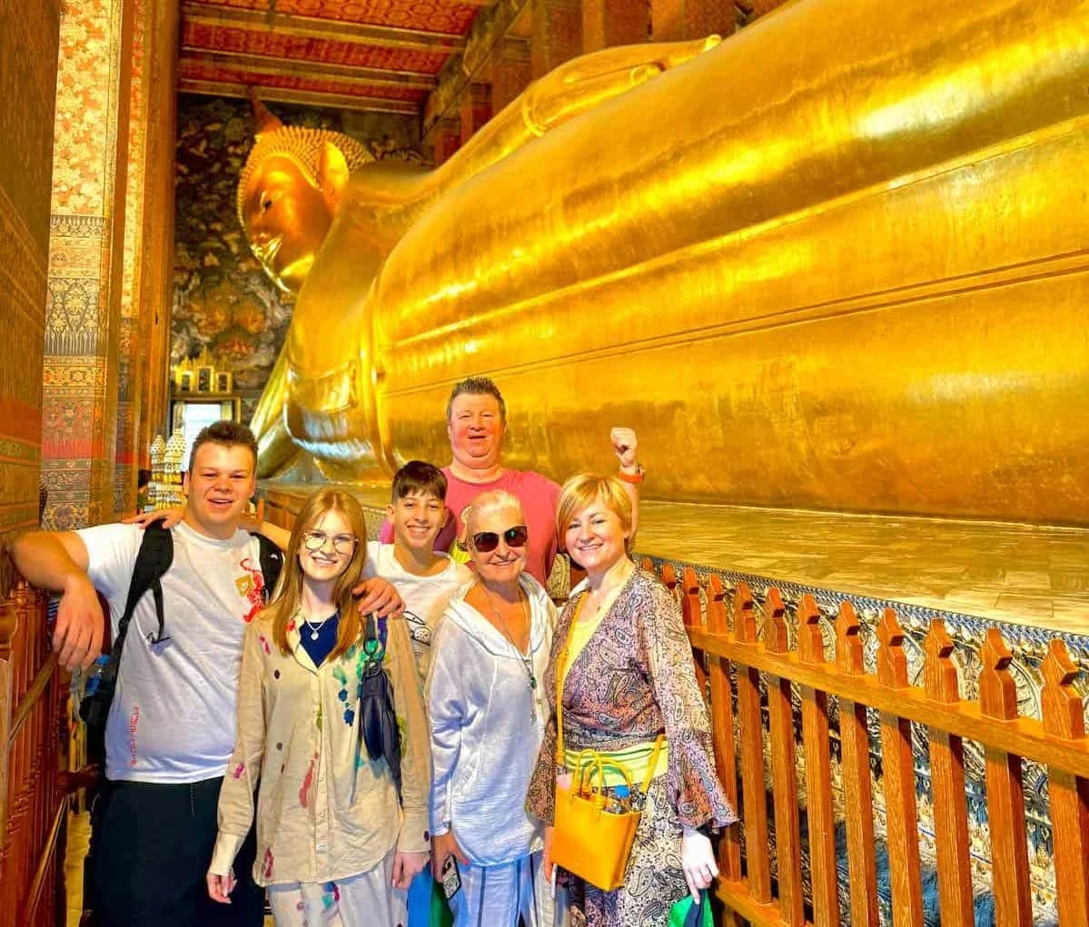 Group of six people posing in front of a massive, reclining golden Buddha statue inside a temple.