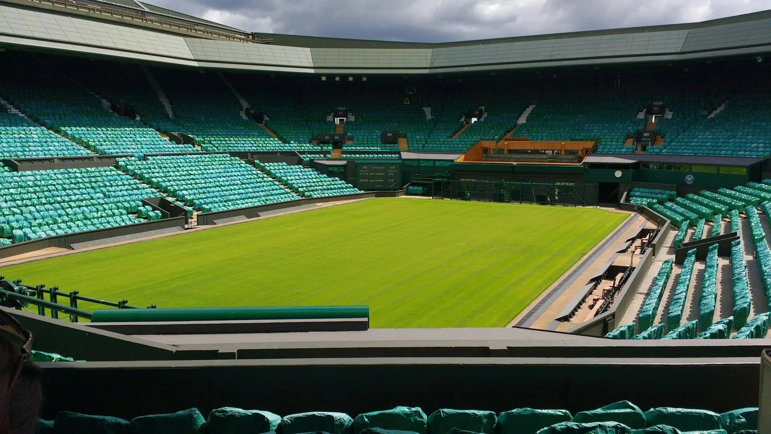 Empty baseball stadium with green grass field and enclosed seating areas covered with teal plastic seats.