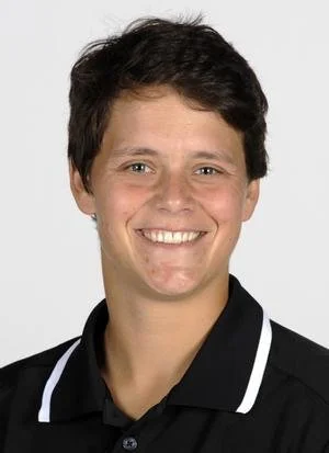 Portrait of a woman with short dark hair, smiling, wearing a black collared shirt with white trim.